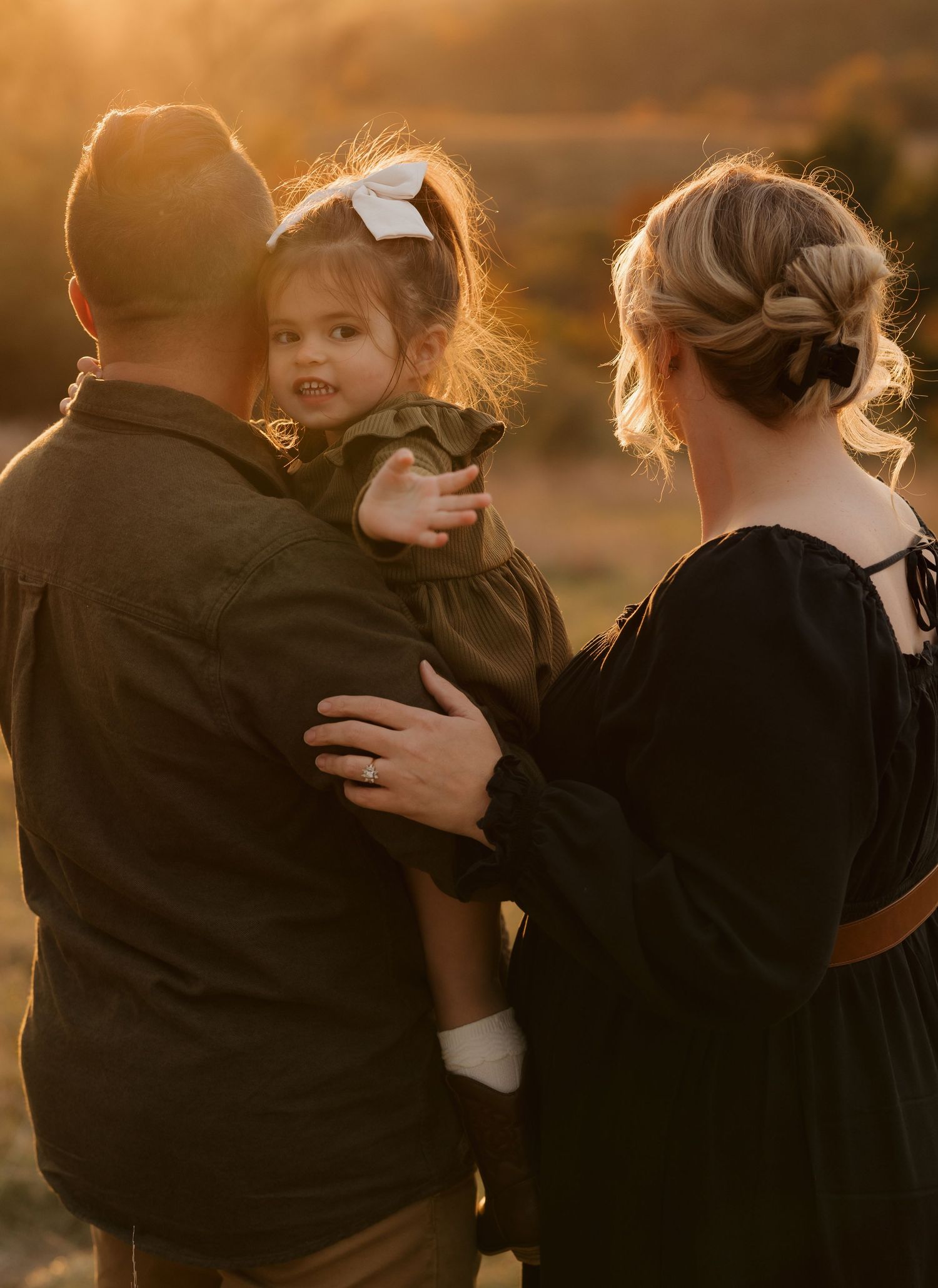 A family embraces in a golden field during sunset.