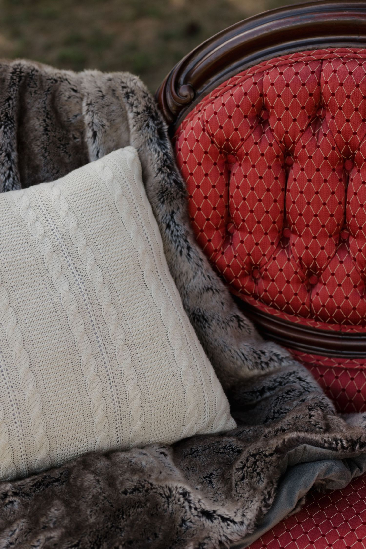Cozy arrangement of knit pillows and fur throws on a red upholstered bench.