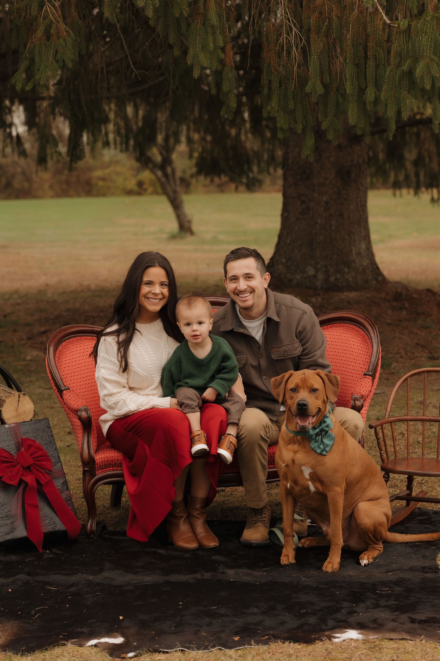 Family sits on a vintage orange couch outdoors with their brown dog wearing a festive bandana.
