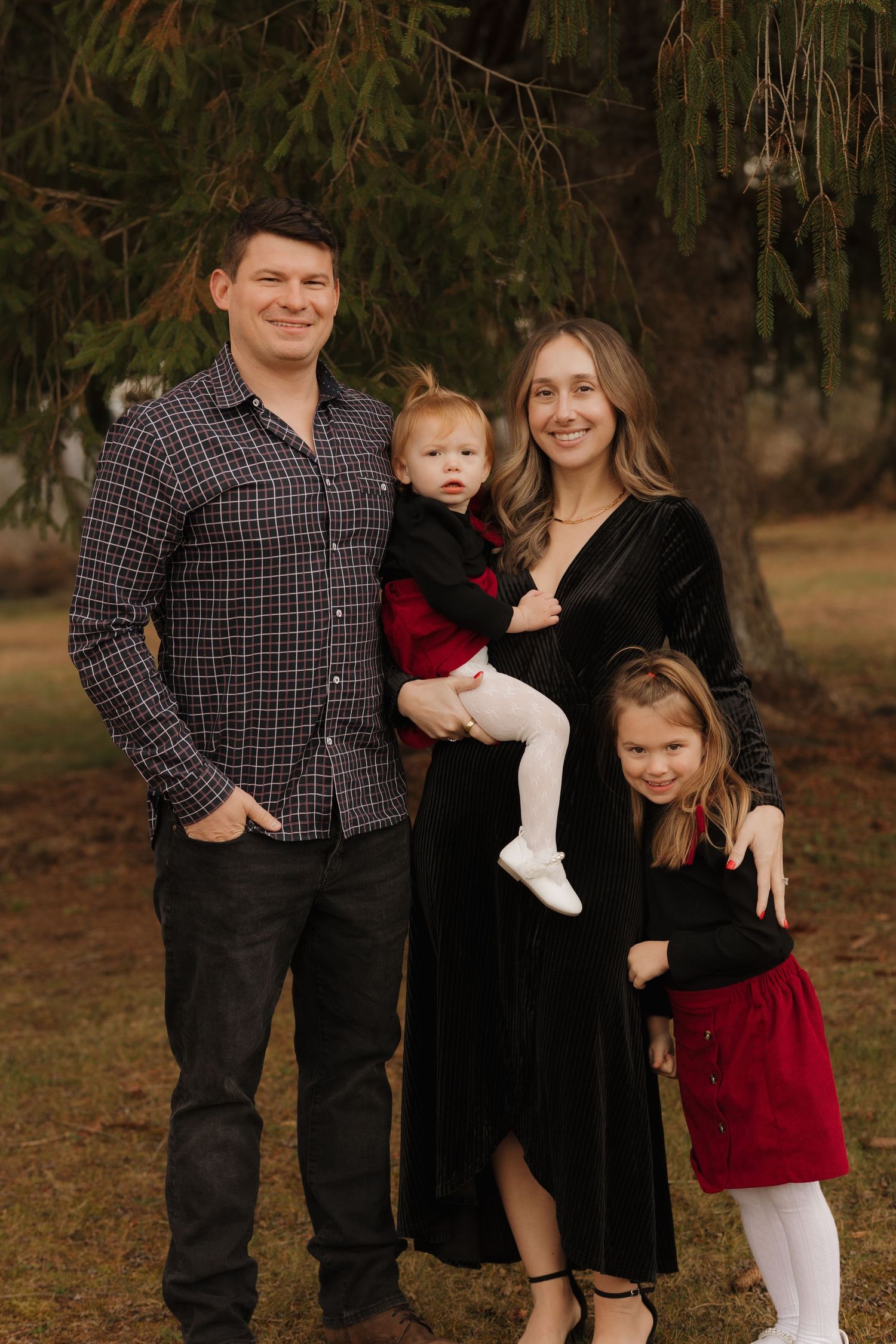 A family of four poses together outdoors wearing coordinated formal attire against an autumn backdrop.