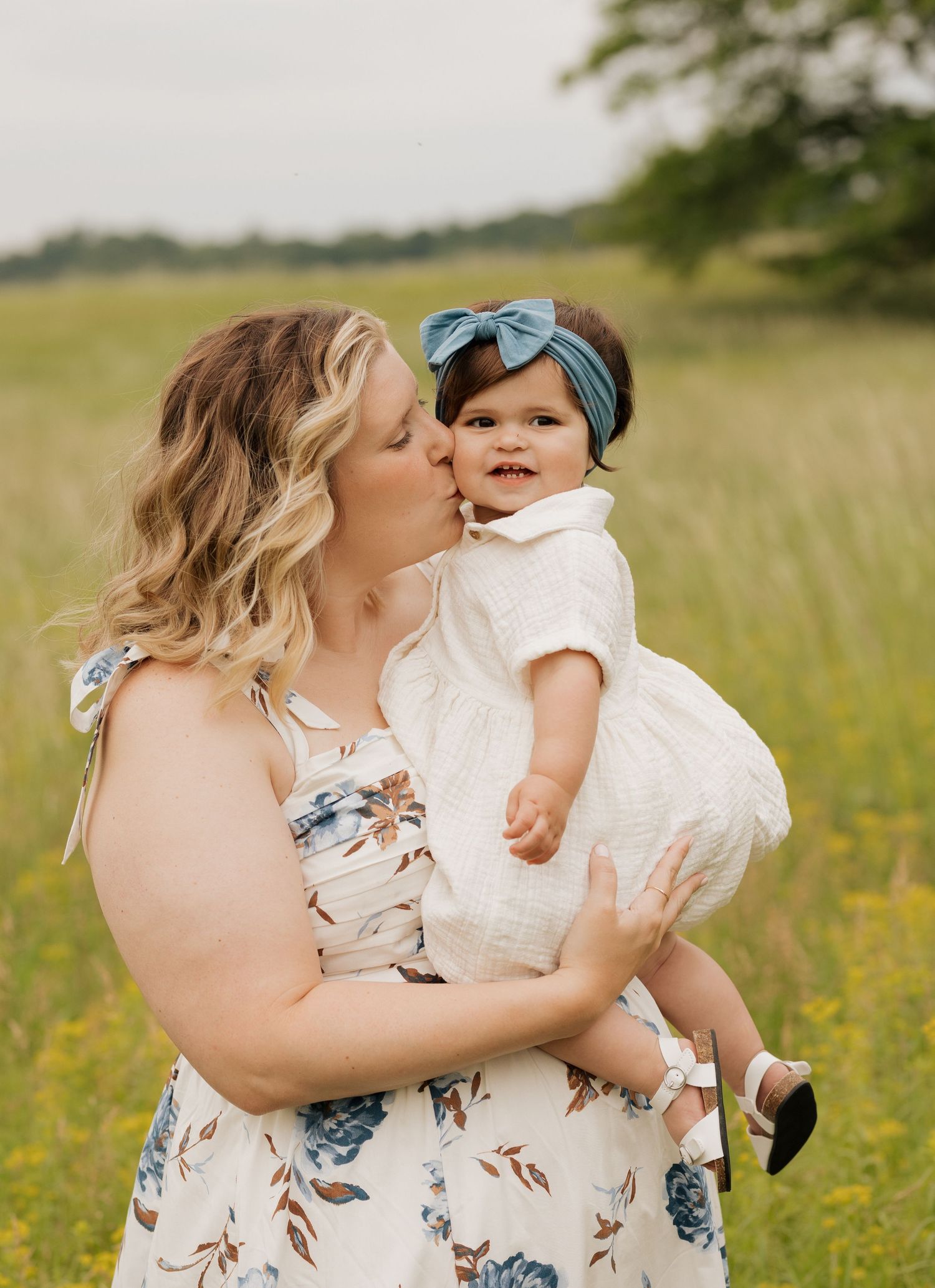 A loving moment between parent and baby in a sunlit meadow with yellow wildflowers.