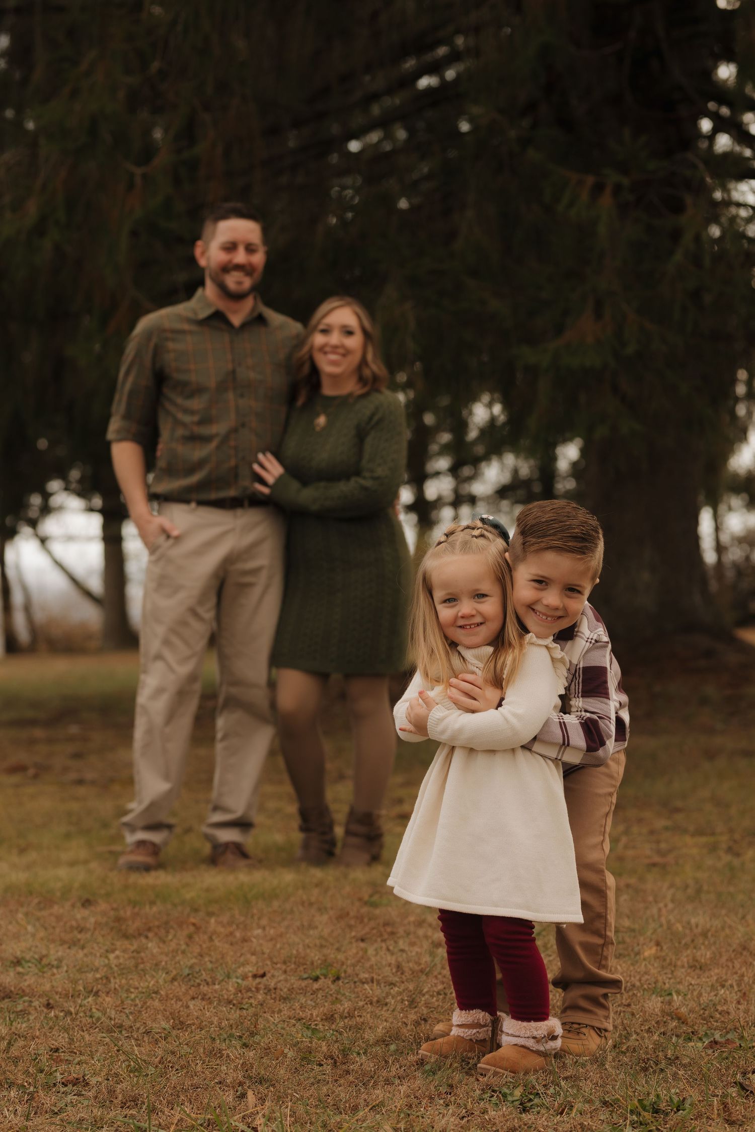 A casual family photo in a wooded setting with children playfully embracing in the foreground.