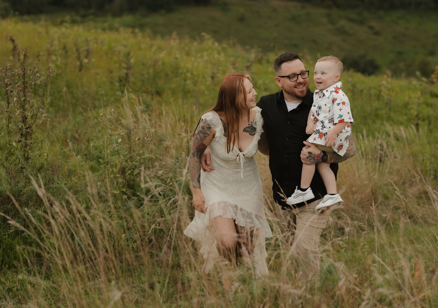 Family wearing coordinated neutral outfits sits together in a sunlit meadow with tall grass during golden hour.