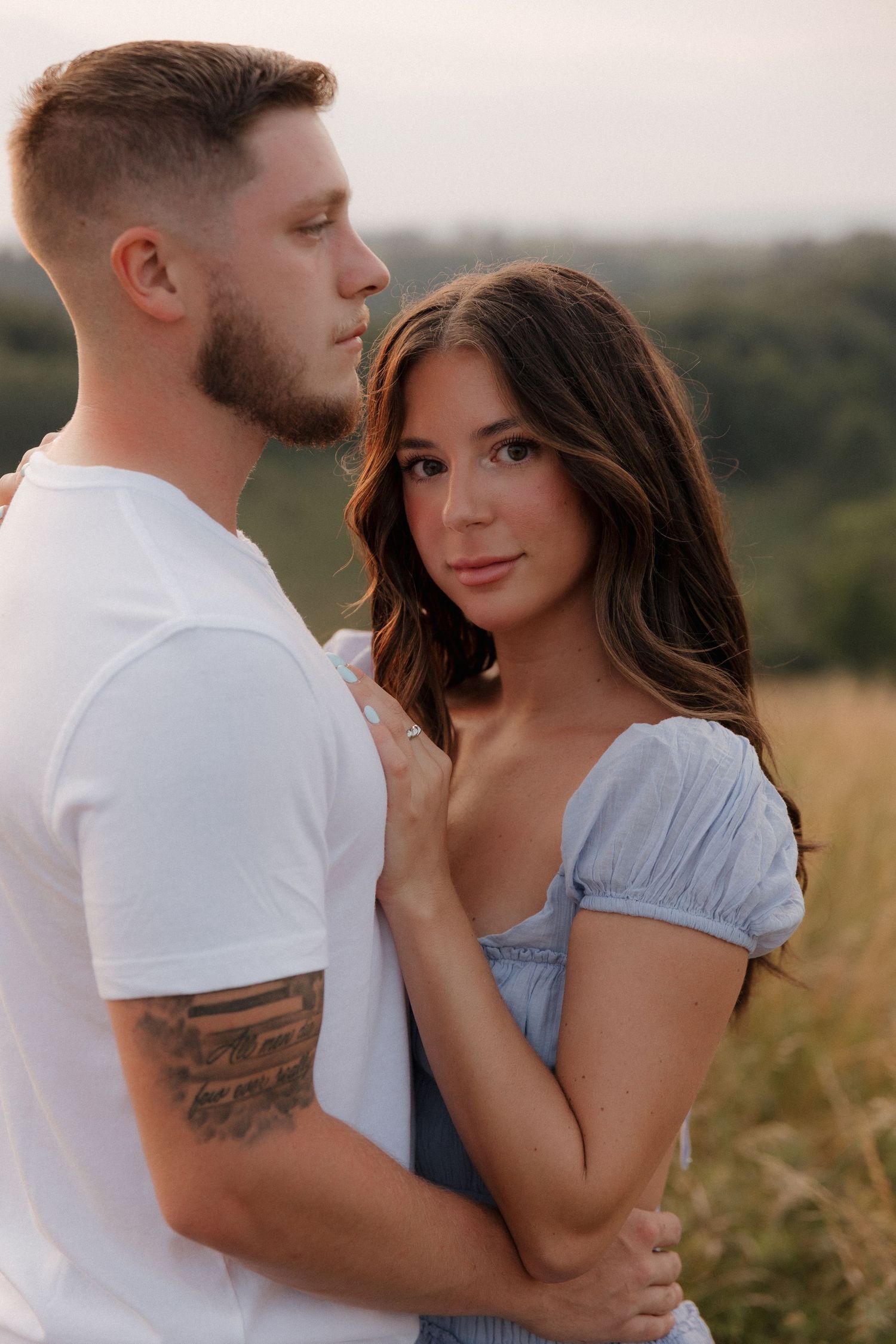 Intimate portrait of a couple in white and blue outfits against a natural outdoor backdrop.