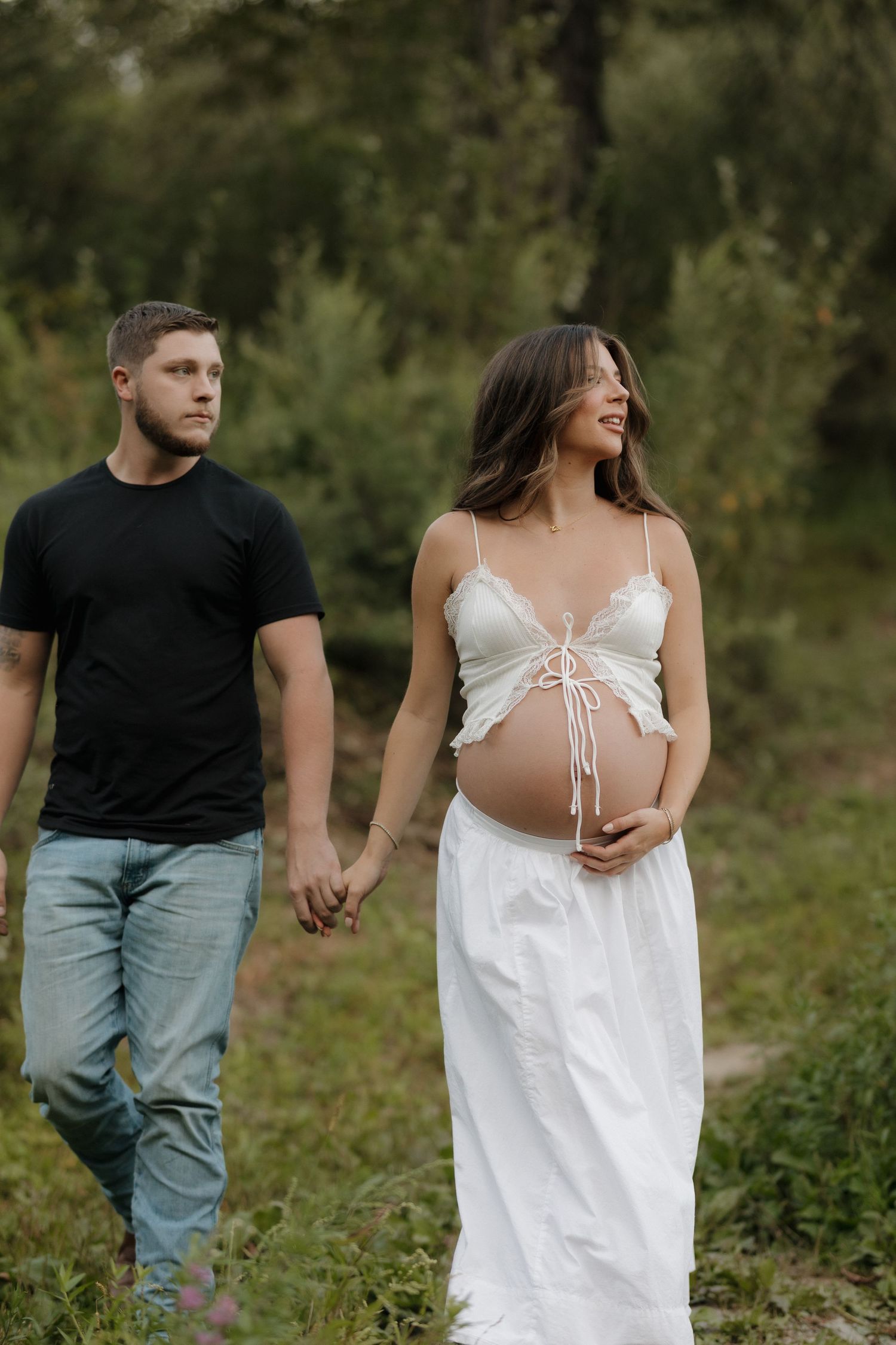 A couple walking hand in hand through a lush green garden setting.