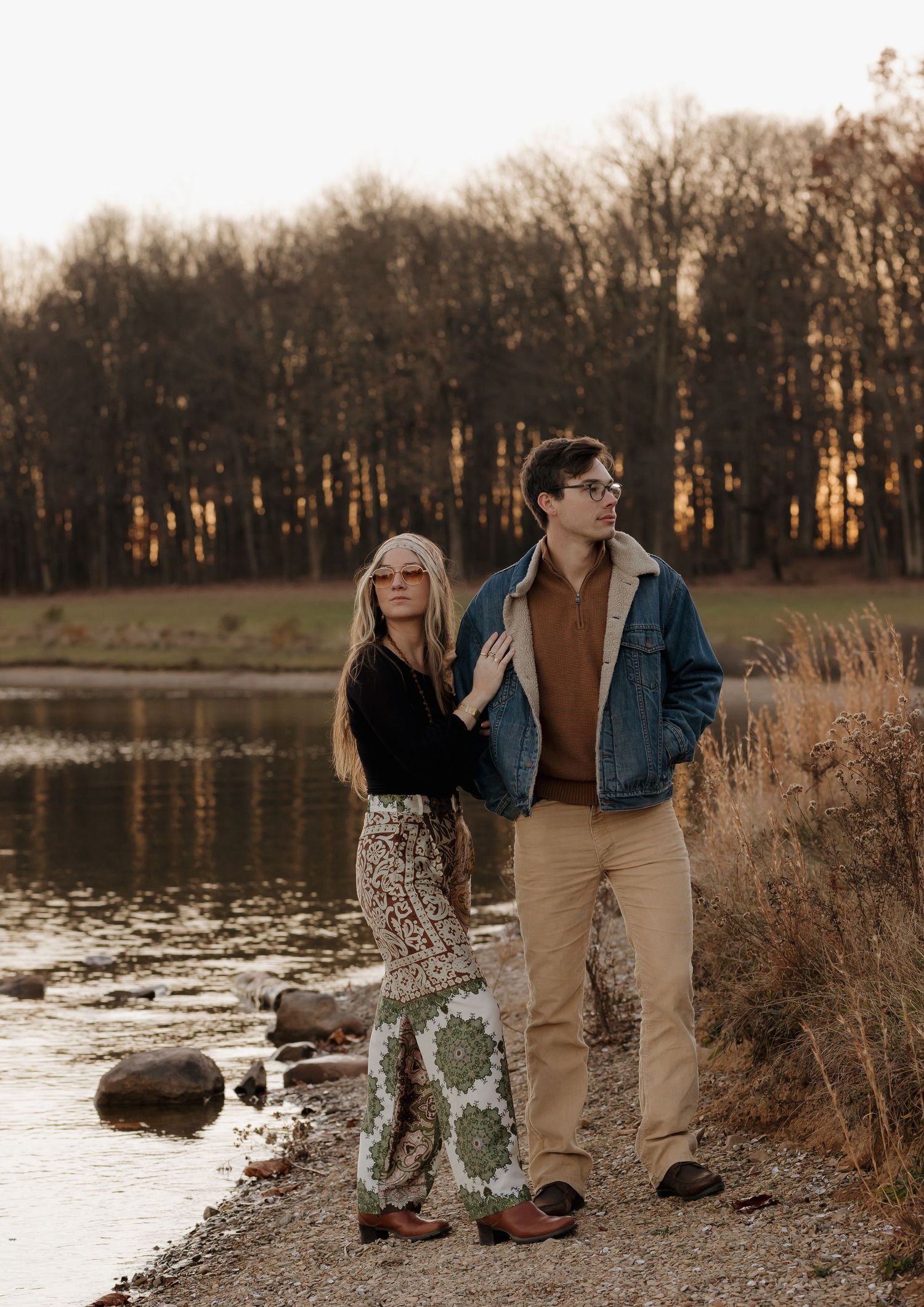 Romantic lakeside photoshoot with couple in casual attire against autumn trees.