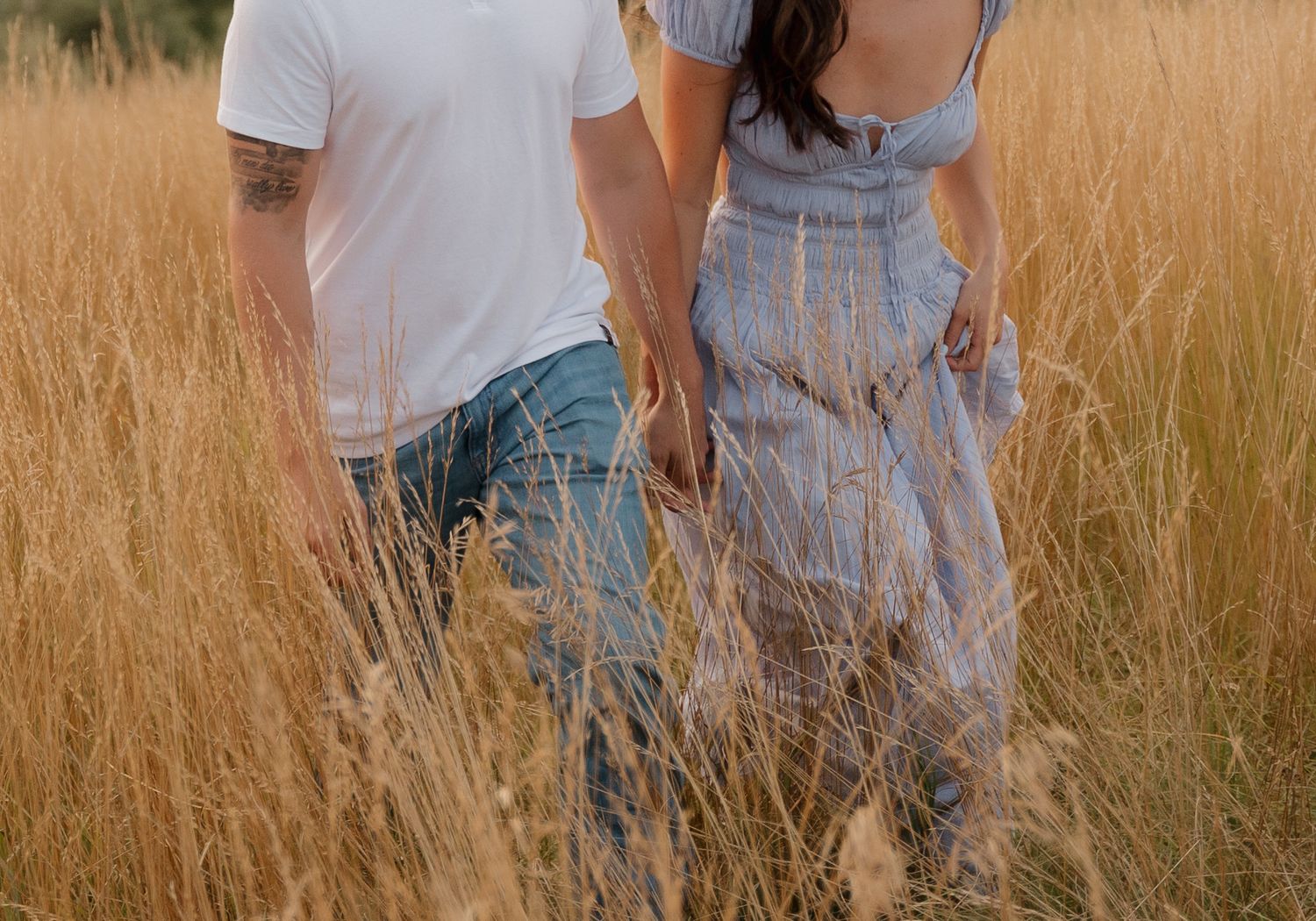 Couple walking through tall golden grass in casual summer outfits.