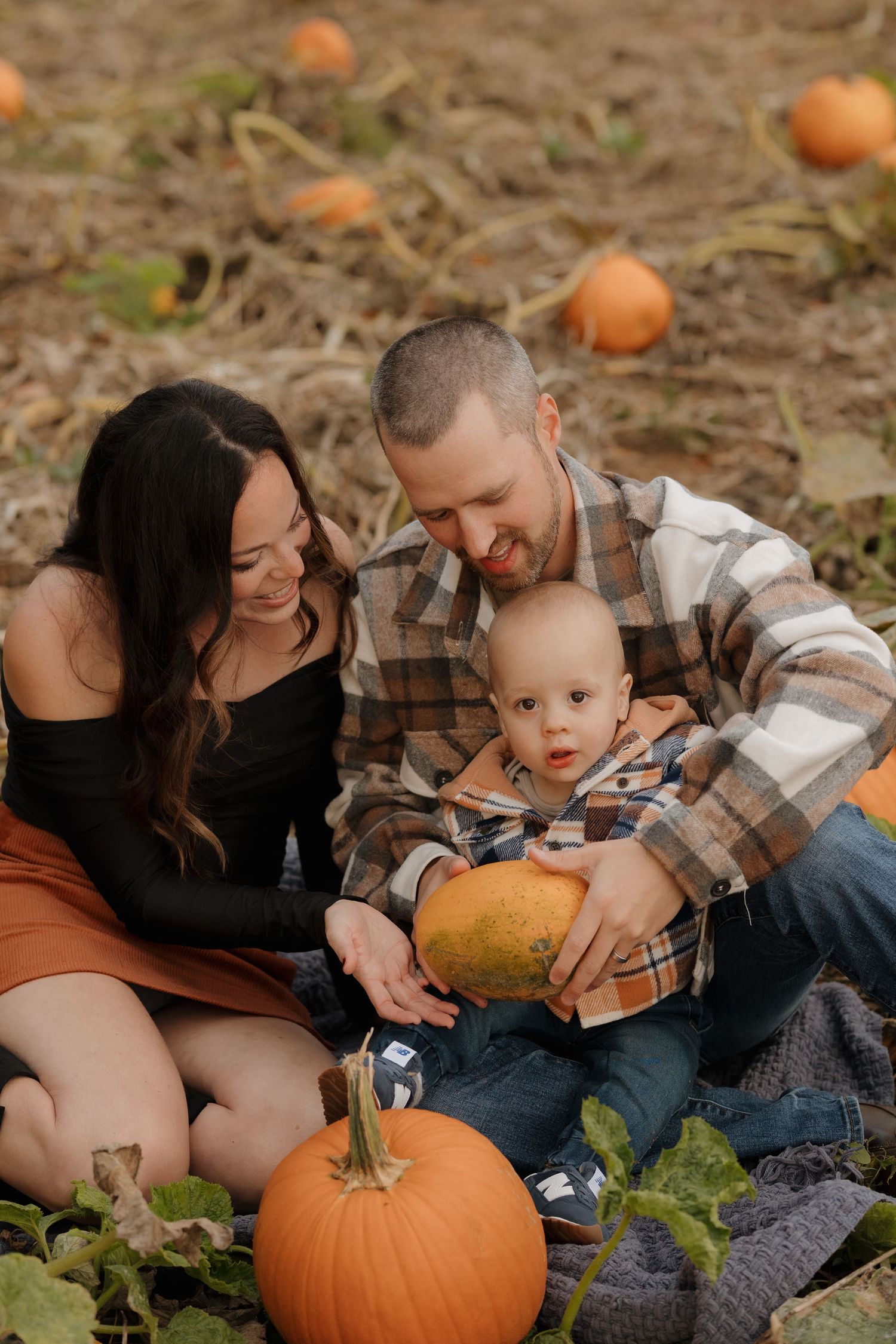 Family enjoys time together in a pumpkin patch during fall.