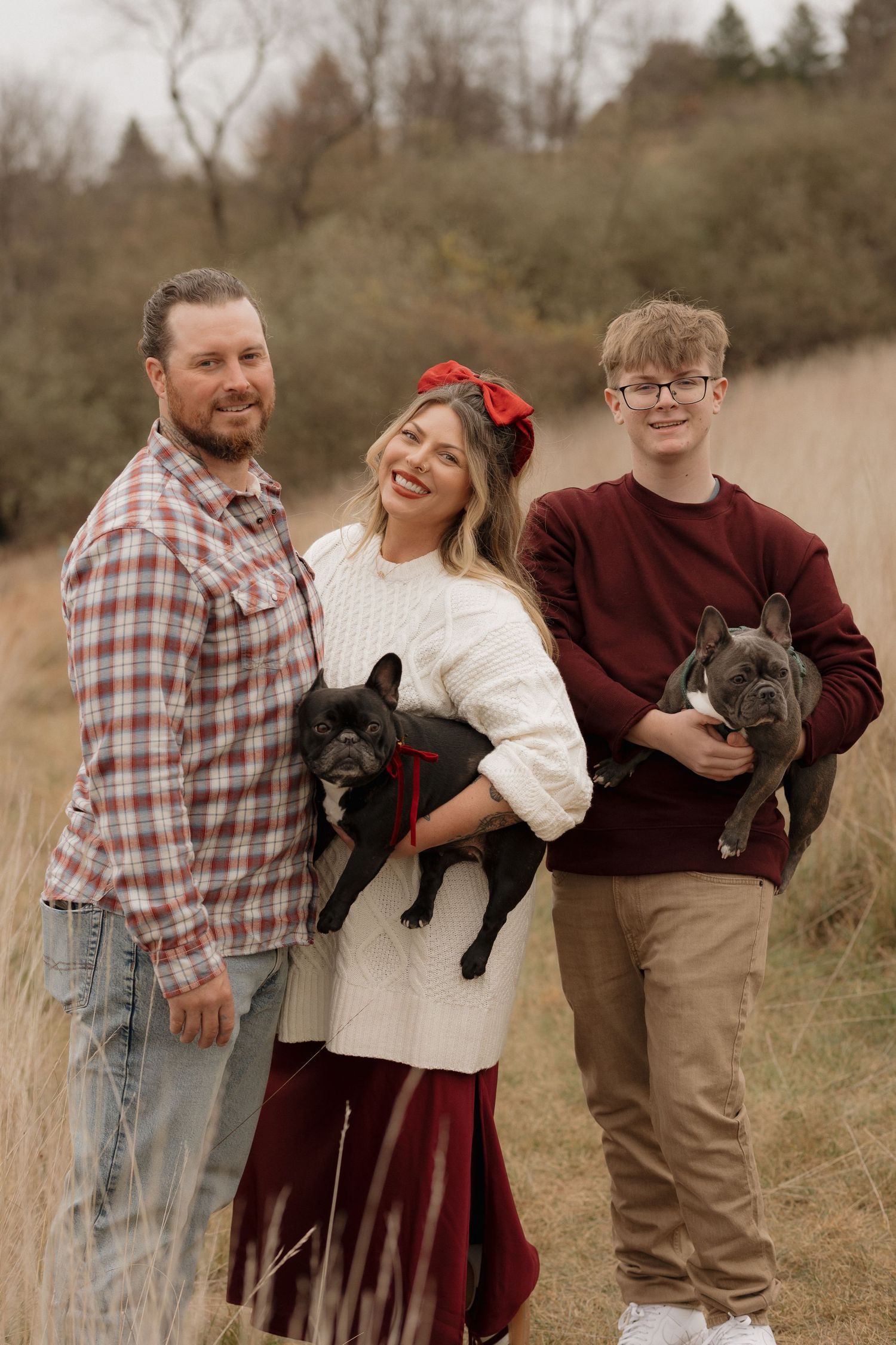 Family posing with their French Bulldogs in rustic outdoor setting.