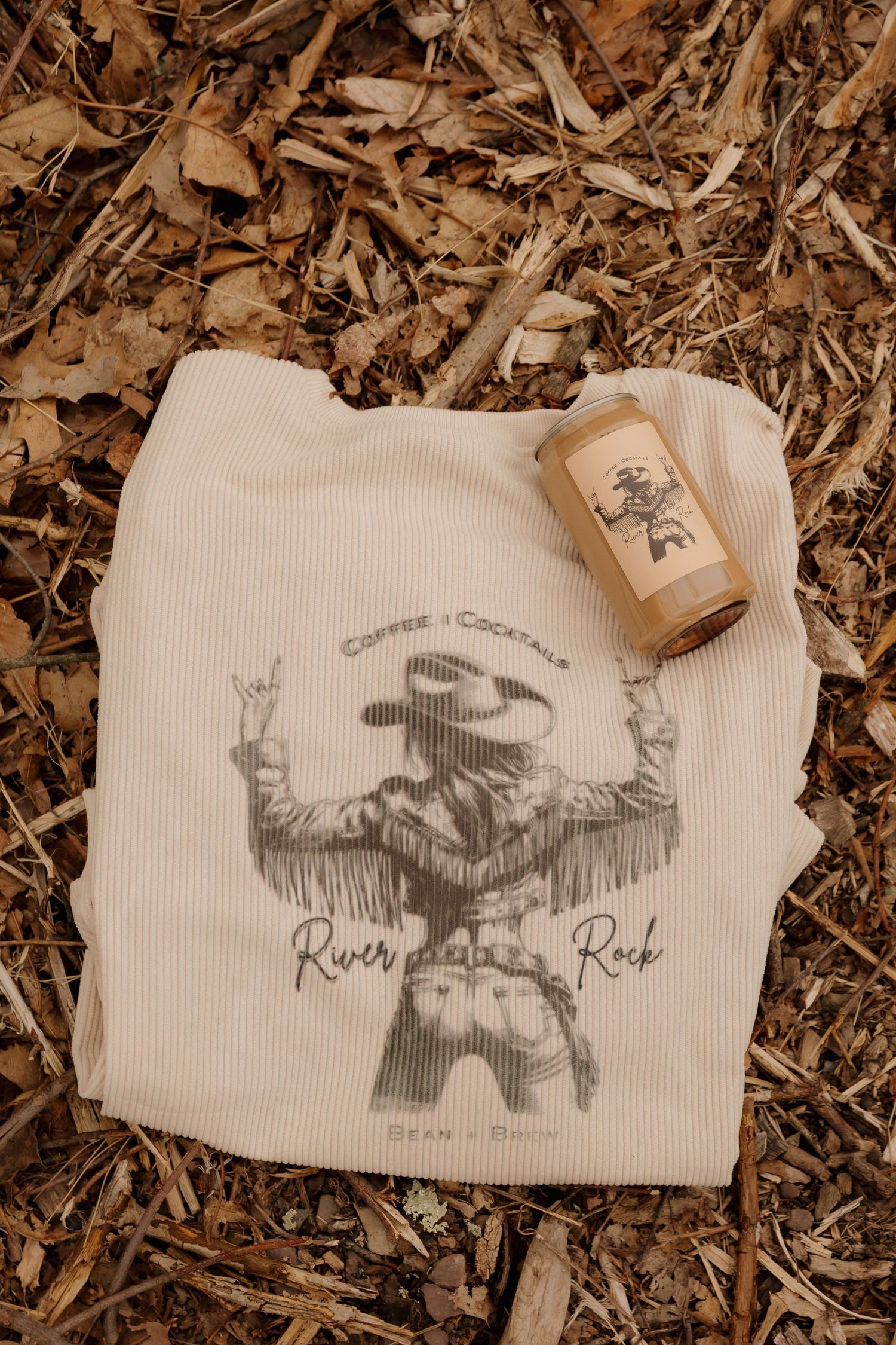 White t-shirt with western cowboy design displayed on natural mulch background.