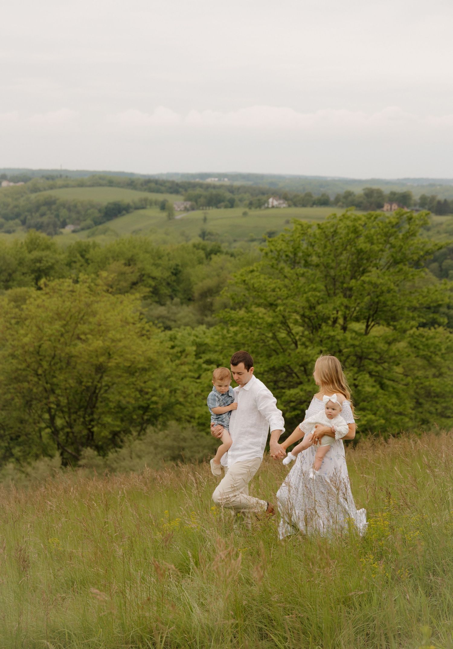 A family walks together through a scenic hilltop meadow with rolling green hills in the background.