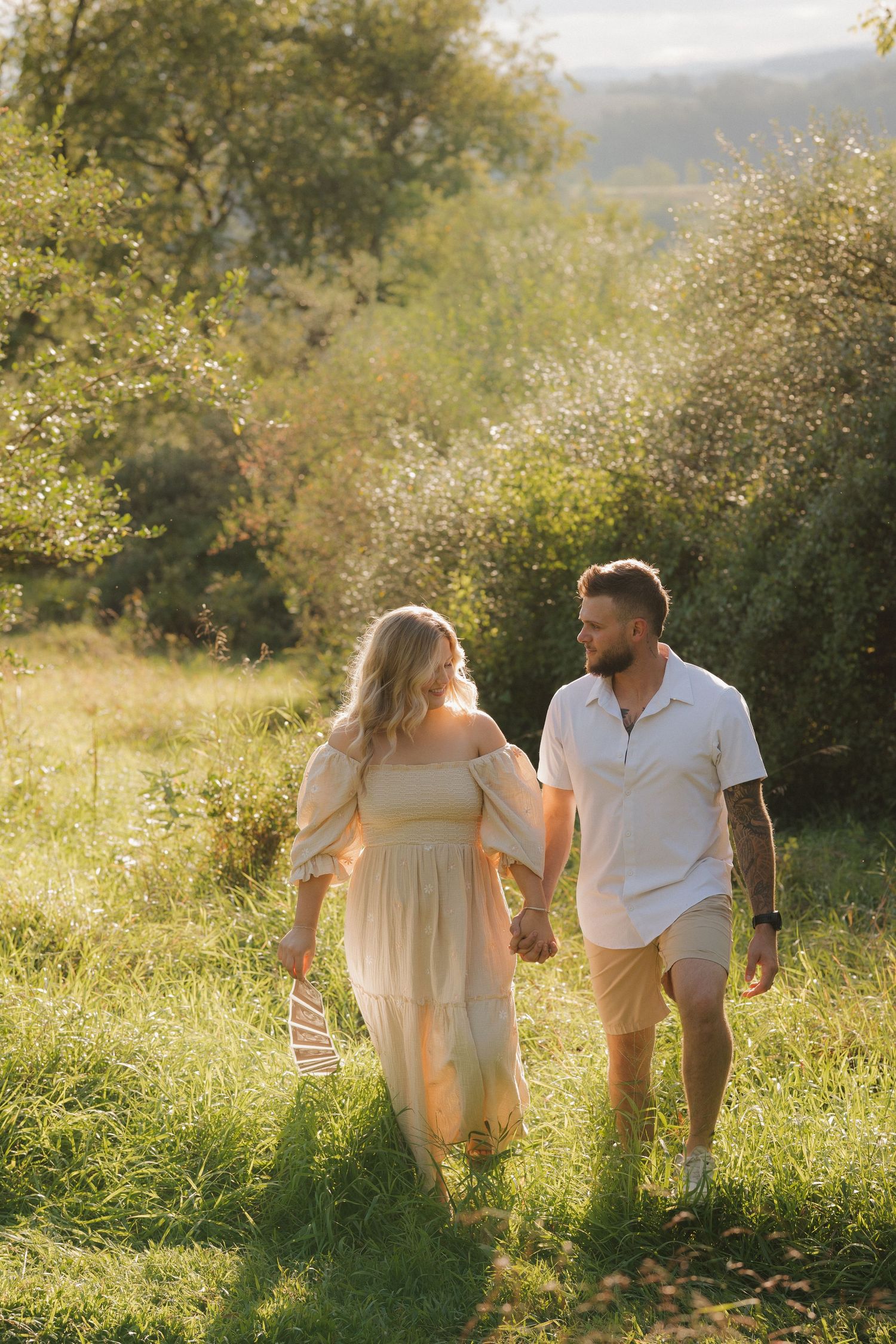 Couple walking through a sun-drenched meadow during golden hour.