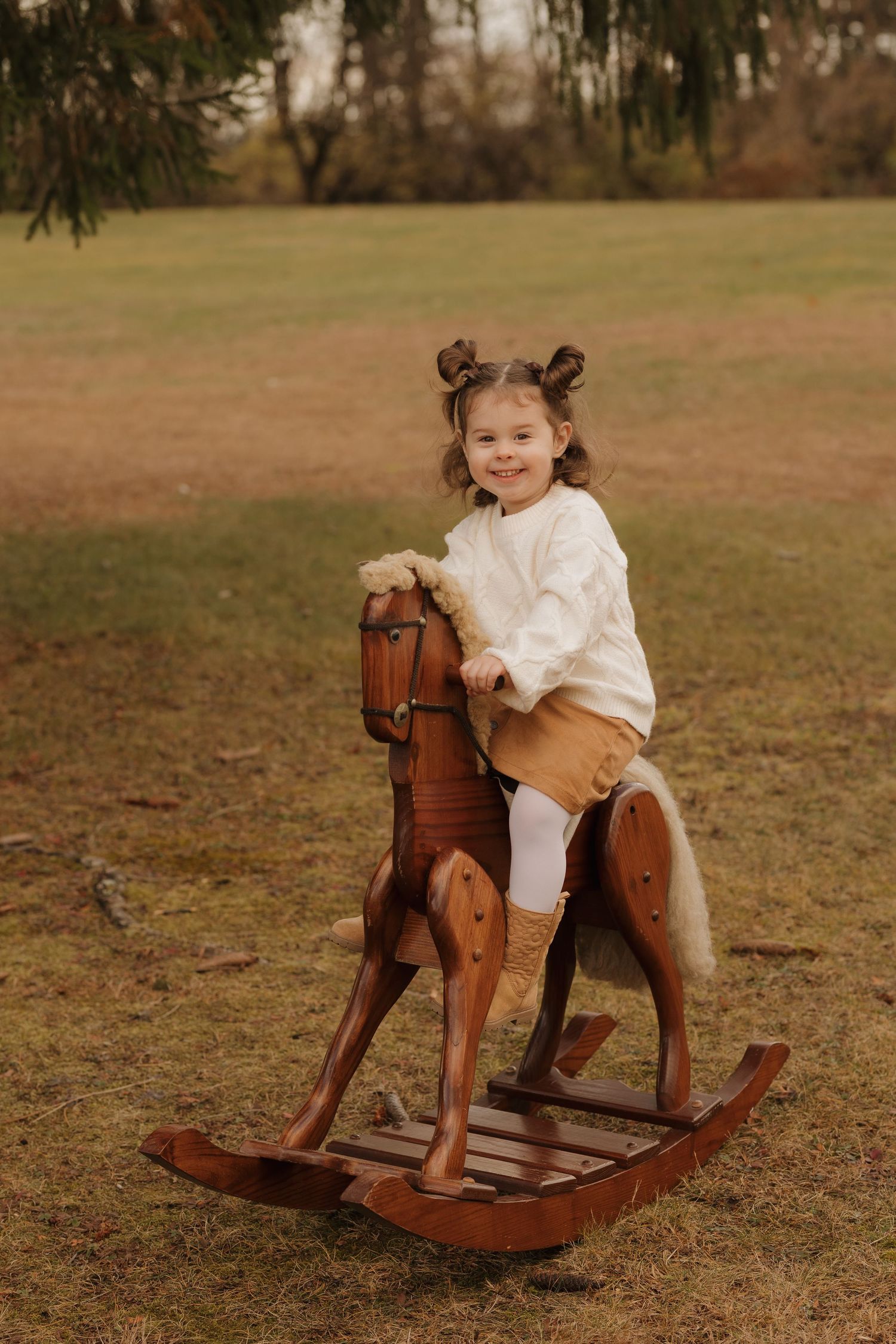 A wooden rocking horse provides entertainment on a grassy field during a fall photoshoot.