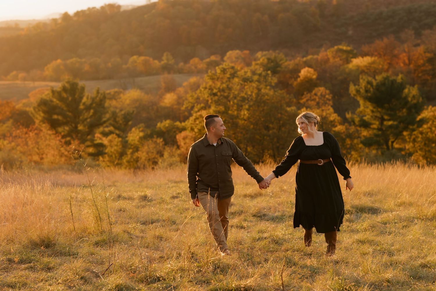 A couple holds hands while running through an autumn field at sunset.