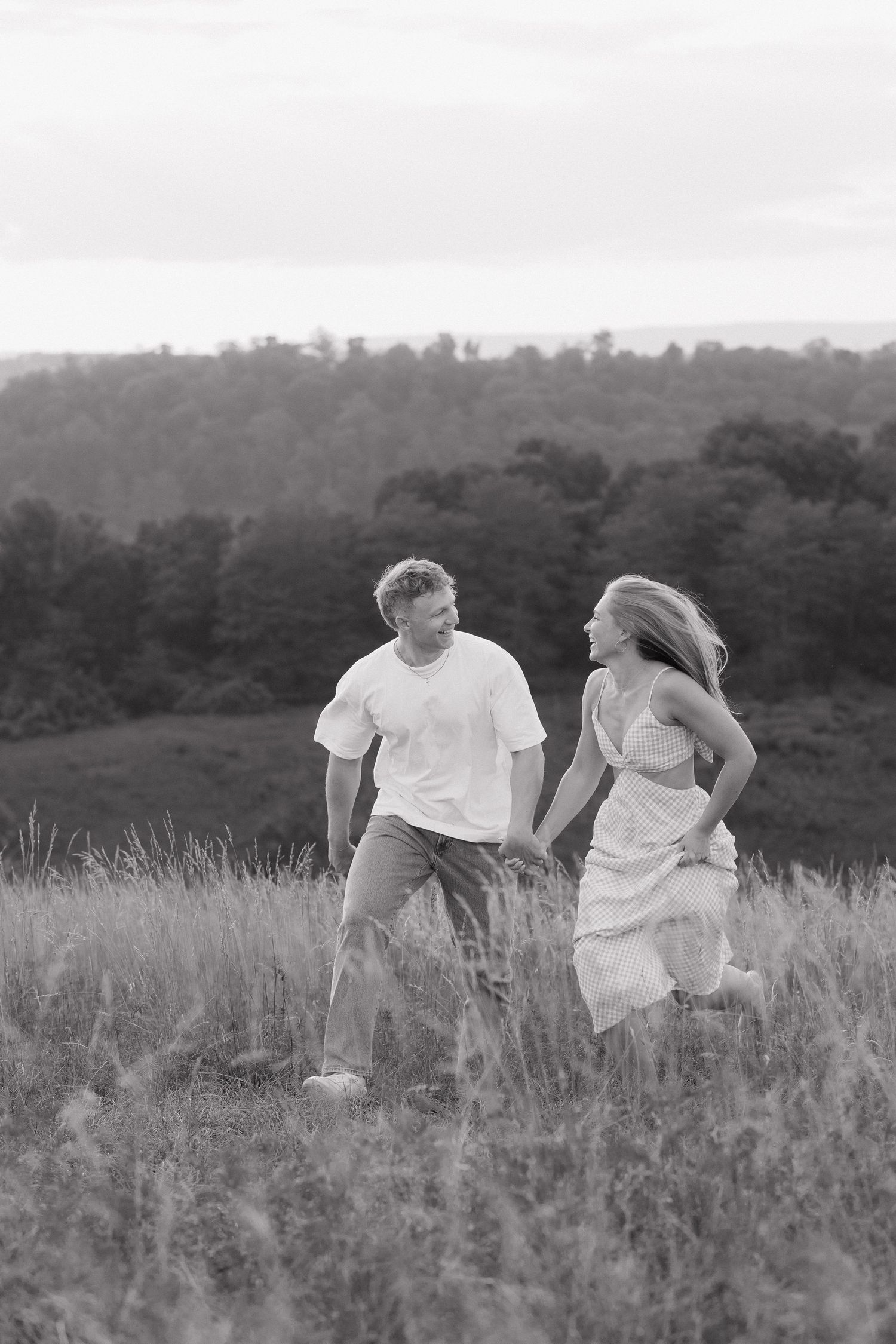 A couple runs playfully through a meadow in black and white.