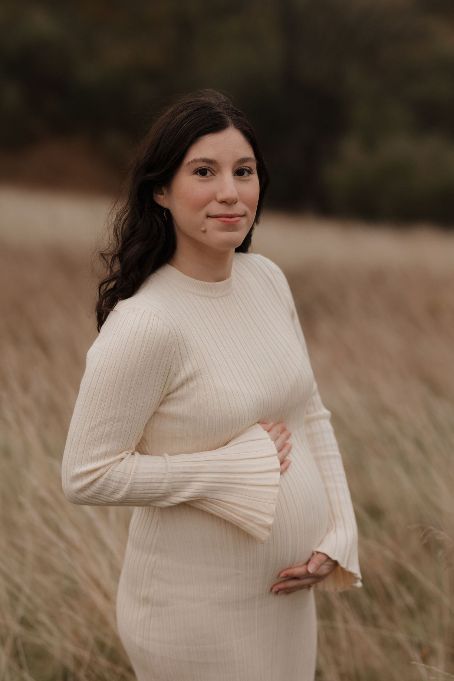 Person in cream sweater poses in tall grass during golden hour.