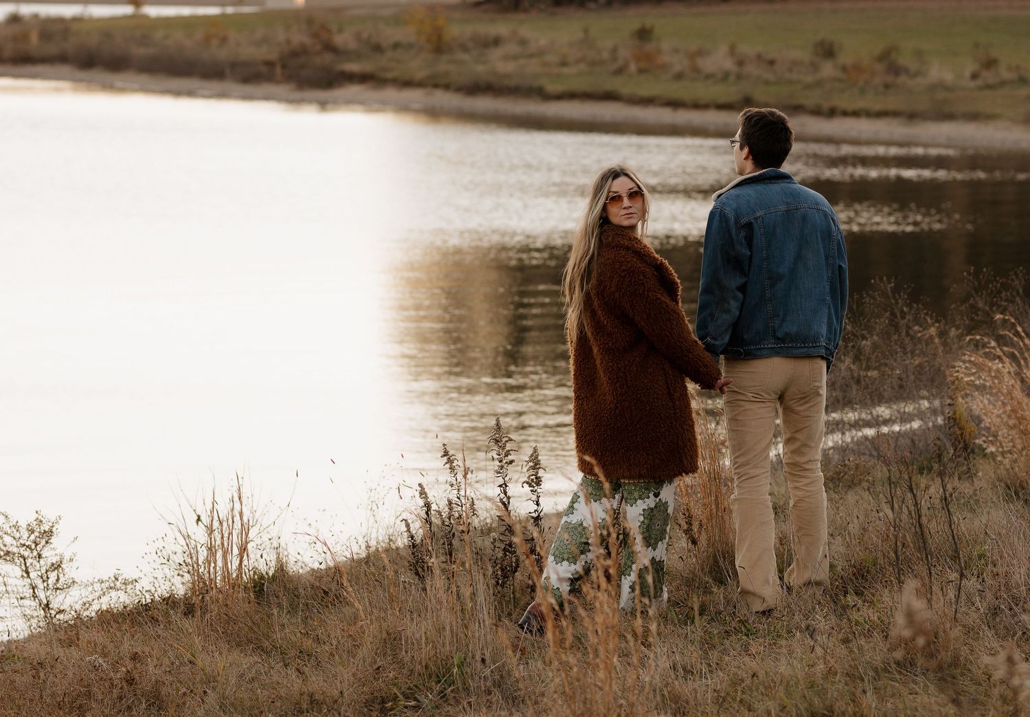 Silhouetted couple walking along lakeside path during golden hour.
