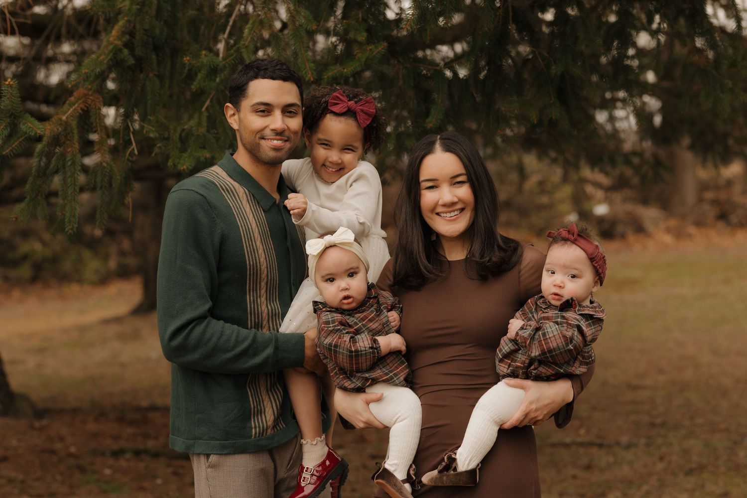 A family of five poses outdoors in coordinating brown and neutral outfits during an autumn photoshoot.