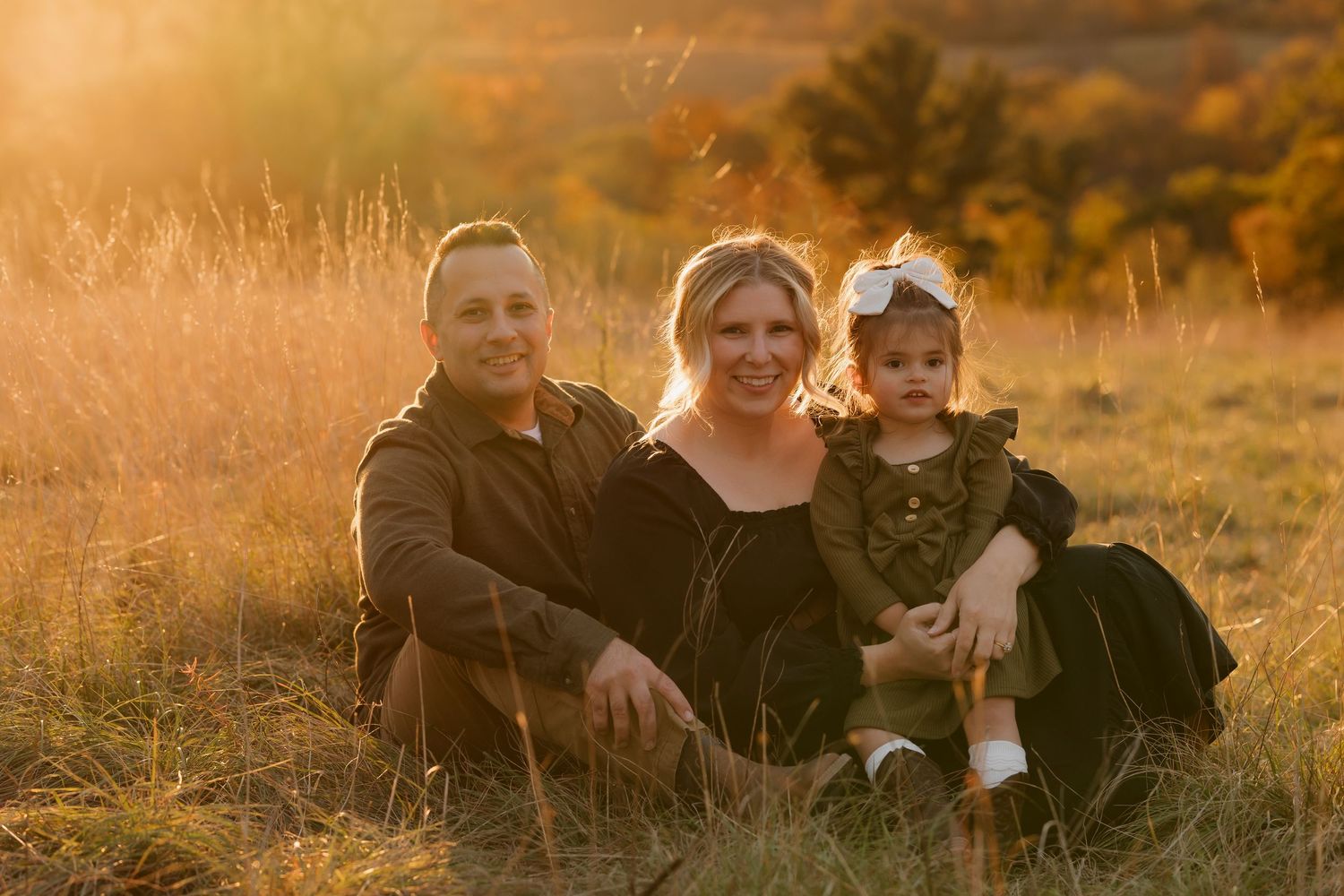 A family sits together in a field during a warm autumn sunset.