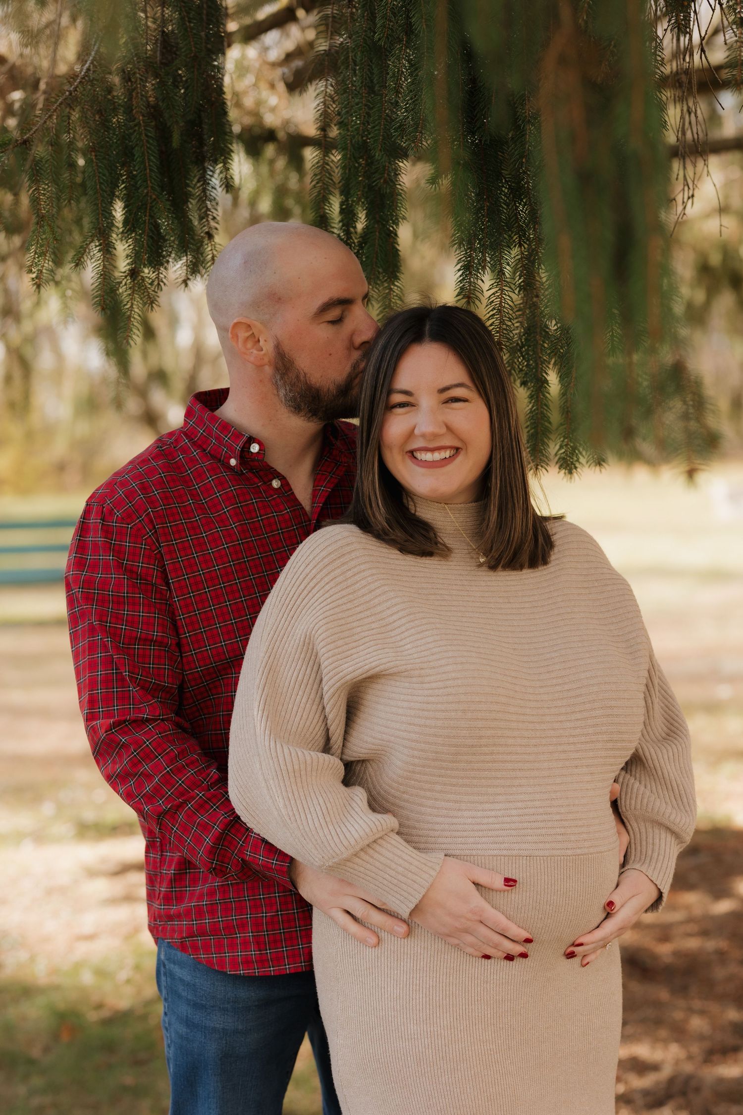 Maternity photo session outdoors with couple in red and beige sweaters.