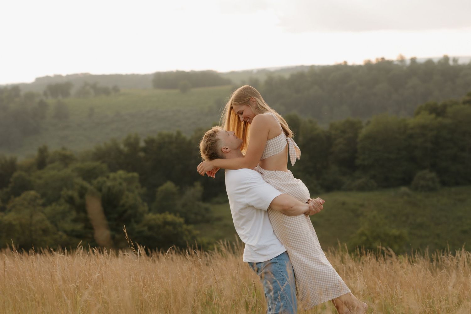A couple embraces in a golden field during sunset.