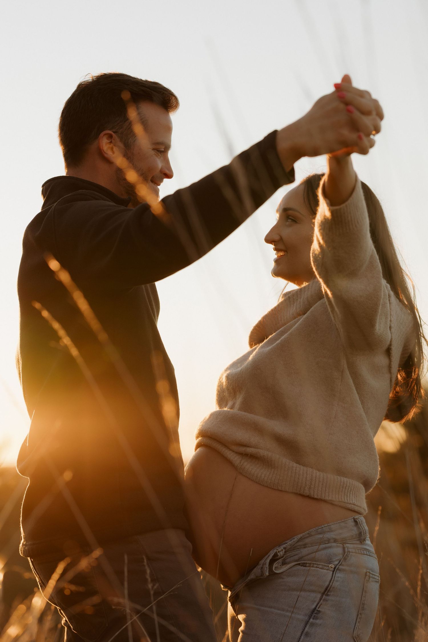 A couple dancing in silhouette against a bright sunset sky.