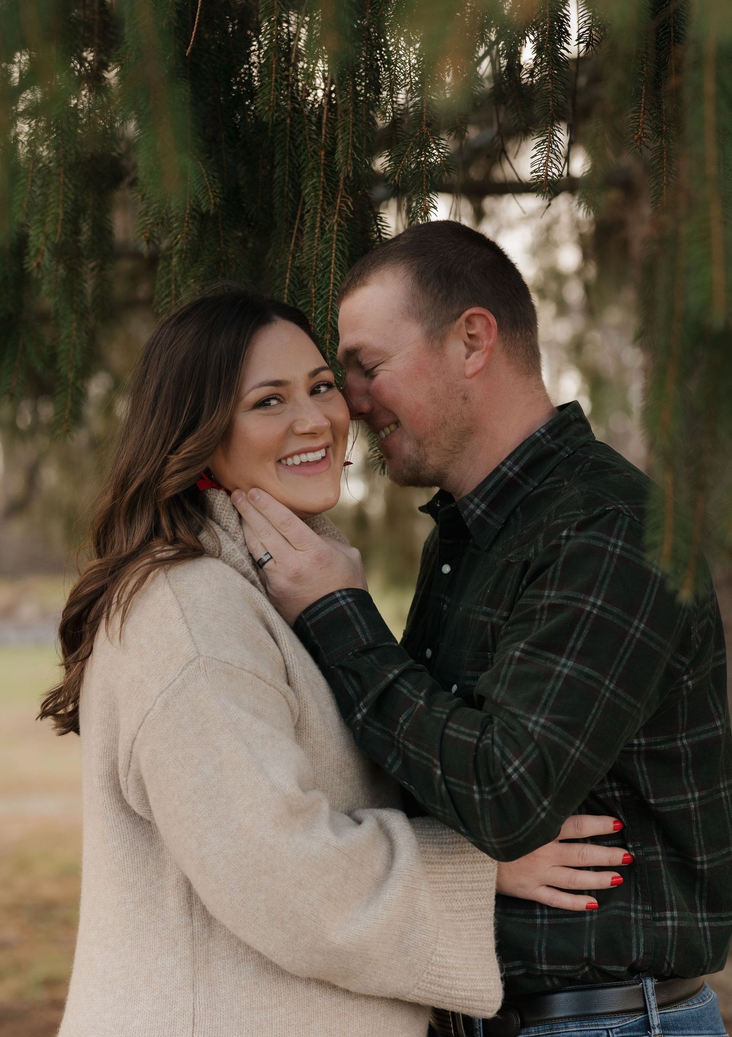A couple shares an intimate moment outdoors with hanging tree branches in the background.