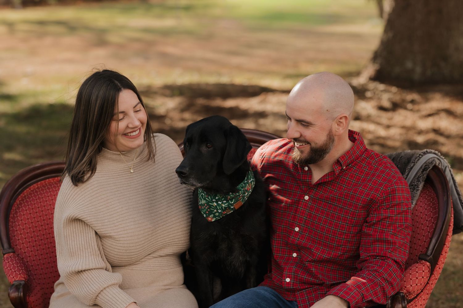 Family sharing candid moments on a red couch during an outdoor photo session.