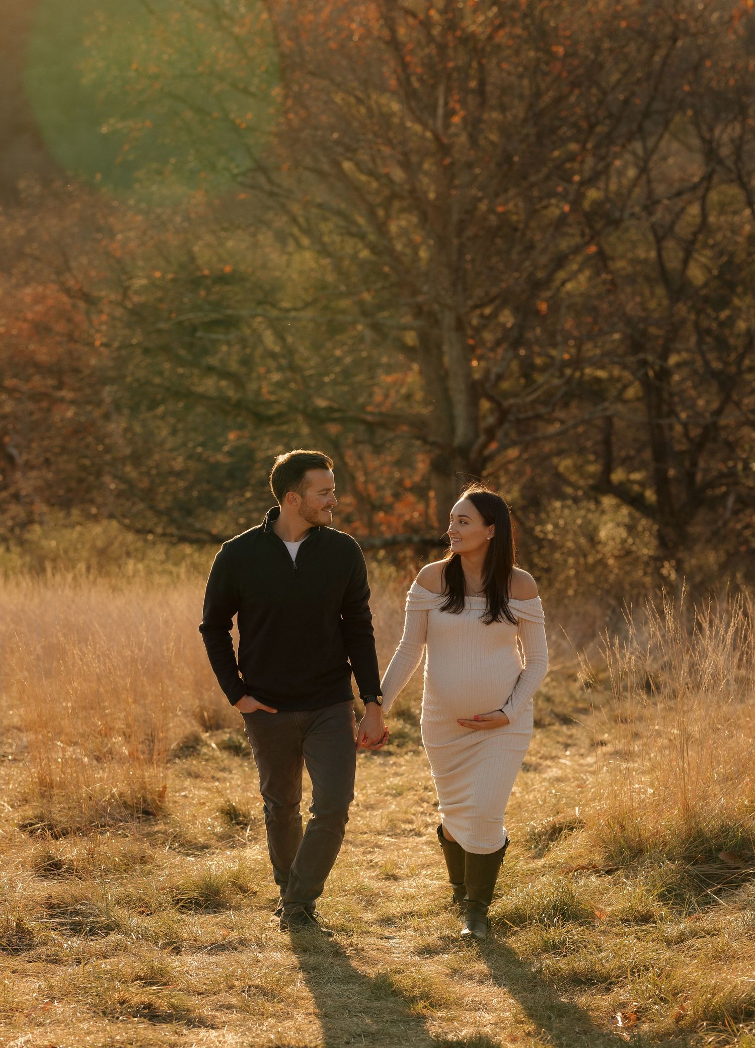 A couple walking together through a sunlit field during golden hour.