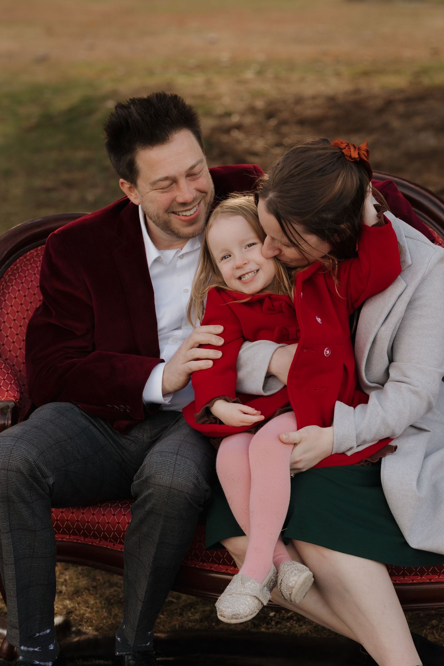 A couple shares intimate moments while relaxing on a red vintage couch outdoors.
