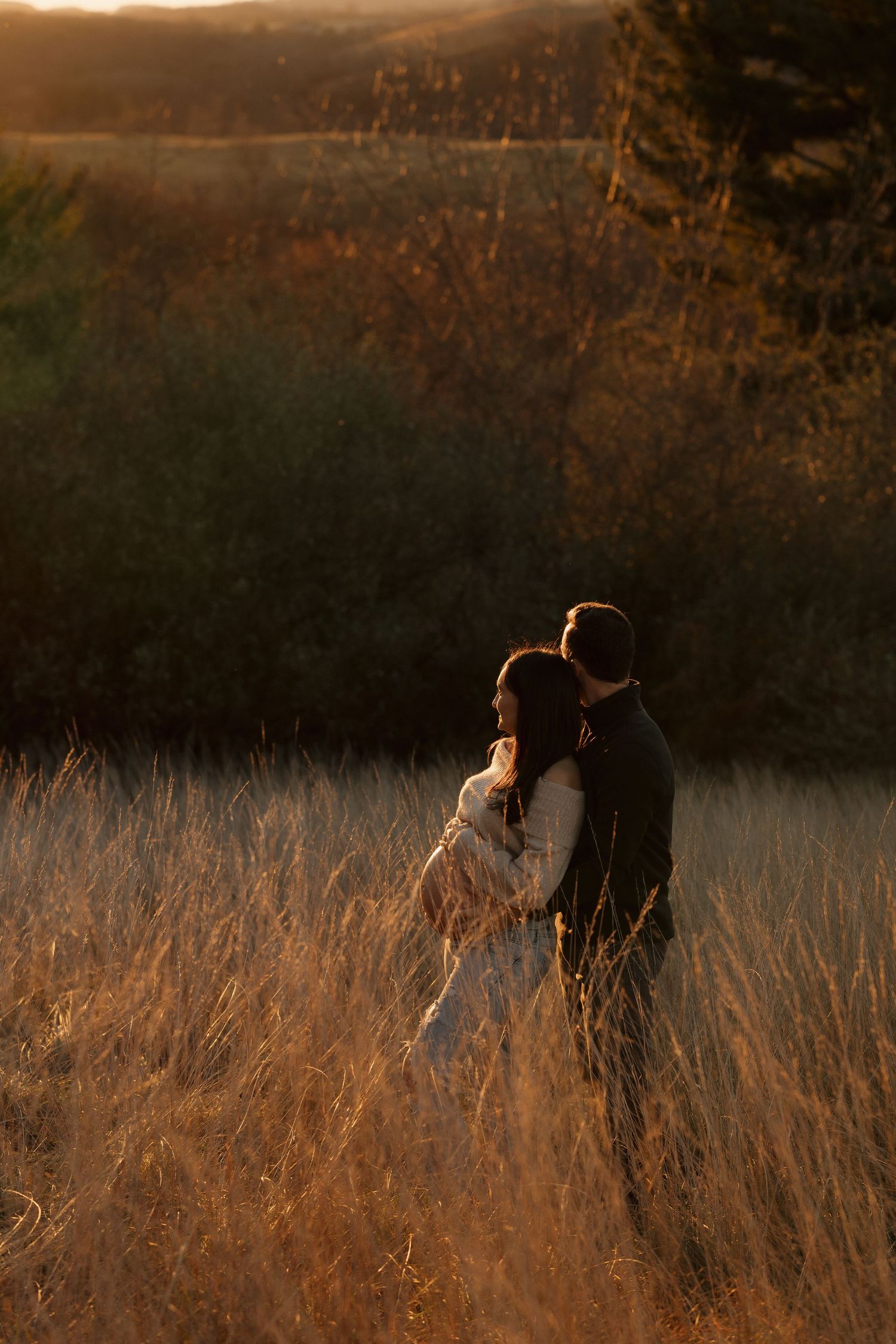 Romantic silhouettes of a couple standing in tall grass during golden hour.