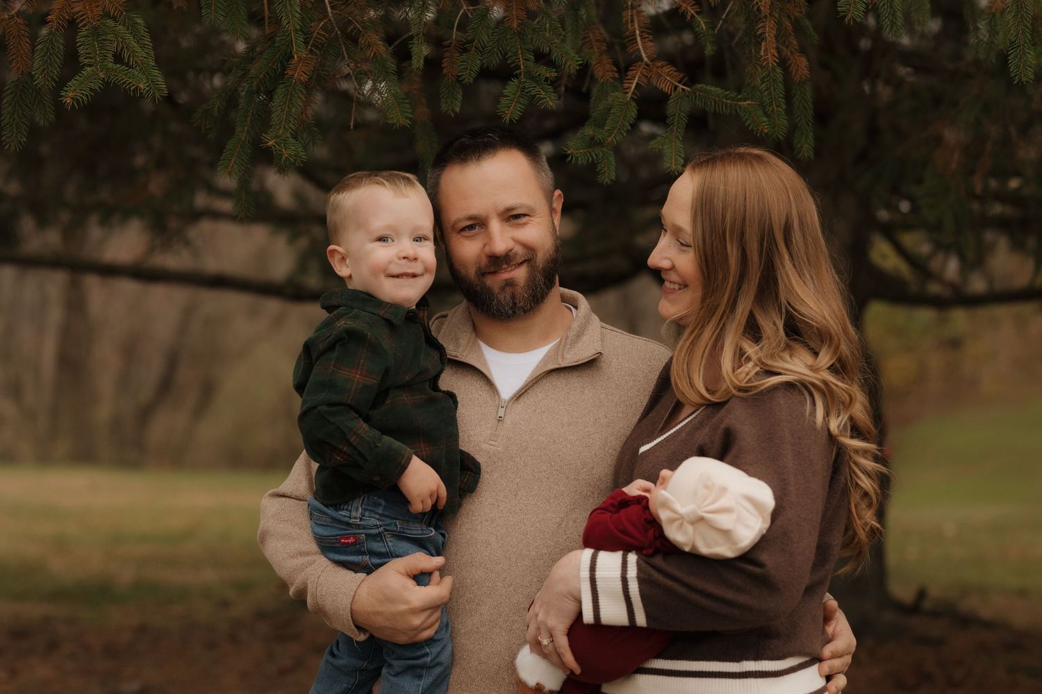 A casual family moment captured outdoors with evergreen trees in the background.