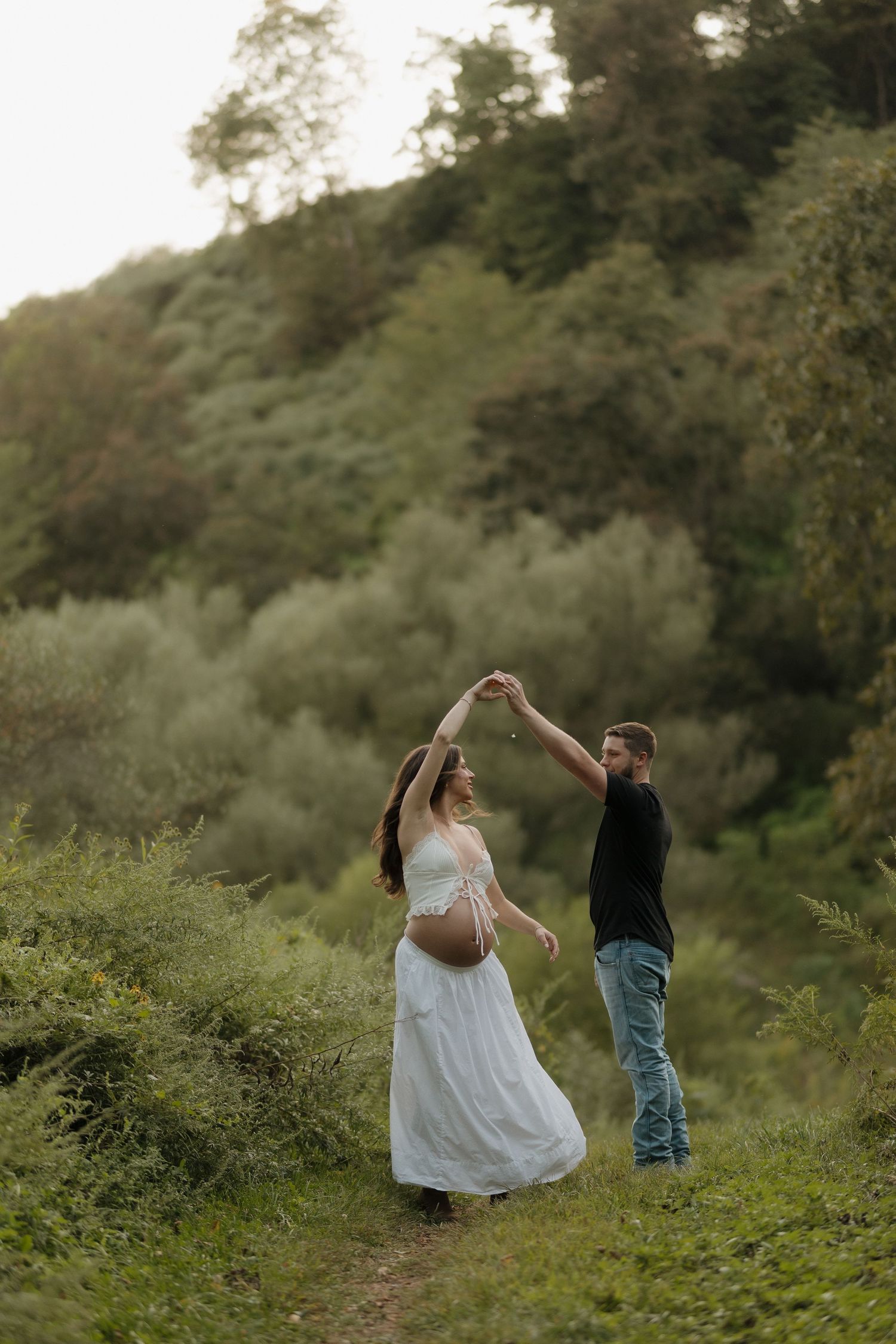 A couple dances together in a lush green field during sunset.