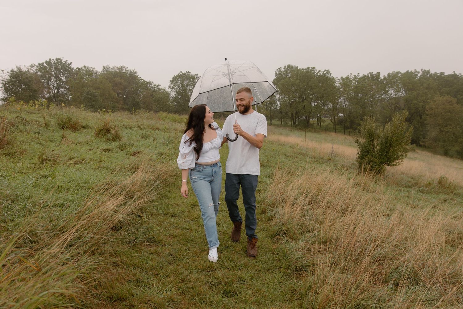 Couple walks together through a rustic field of tall grass on an overcast autumn day.
