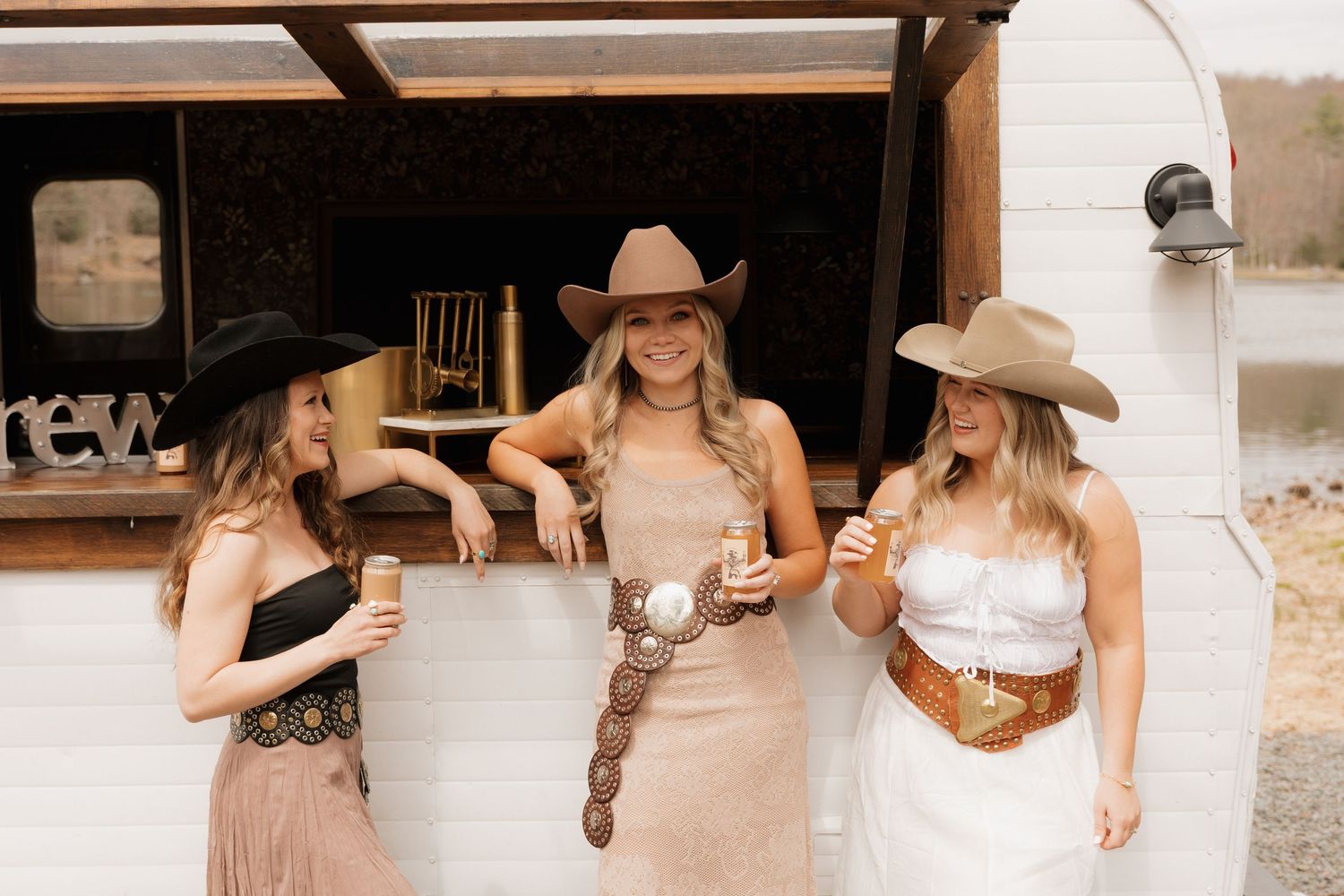Three women in western attire enjoy drinks at an outdoor bar.
