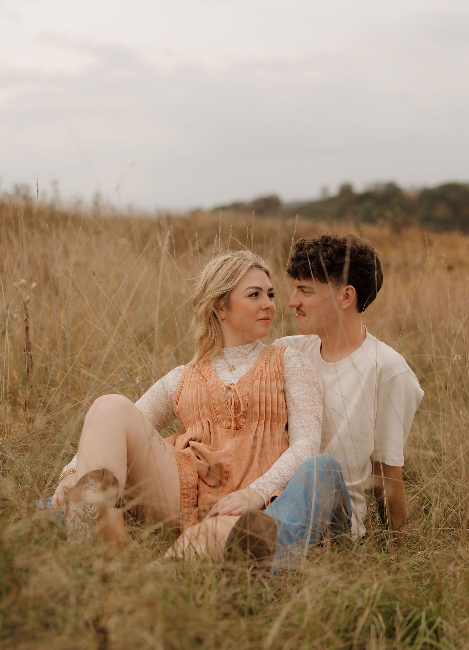 Couple sitting together in tall golden grass field during sunset in warm vintage tones.