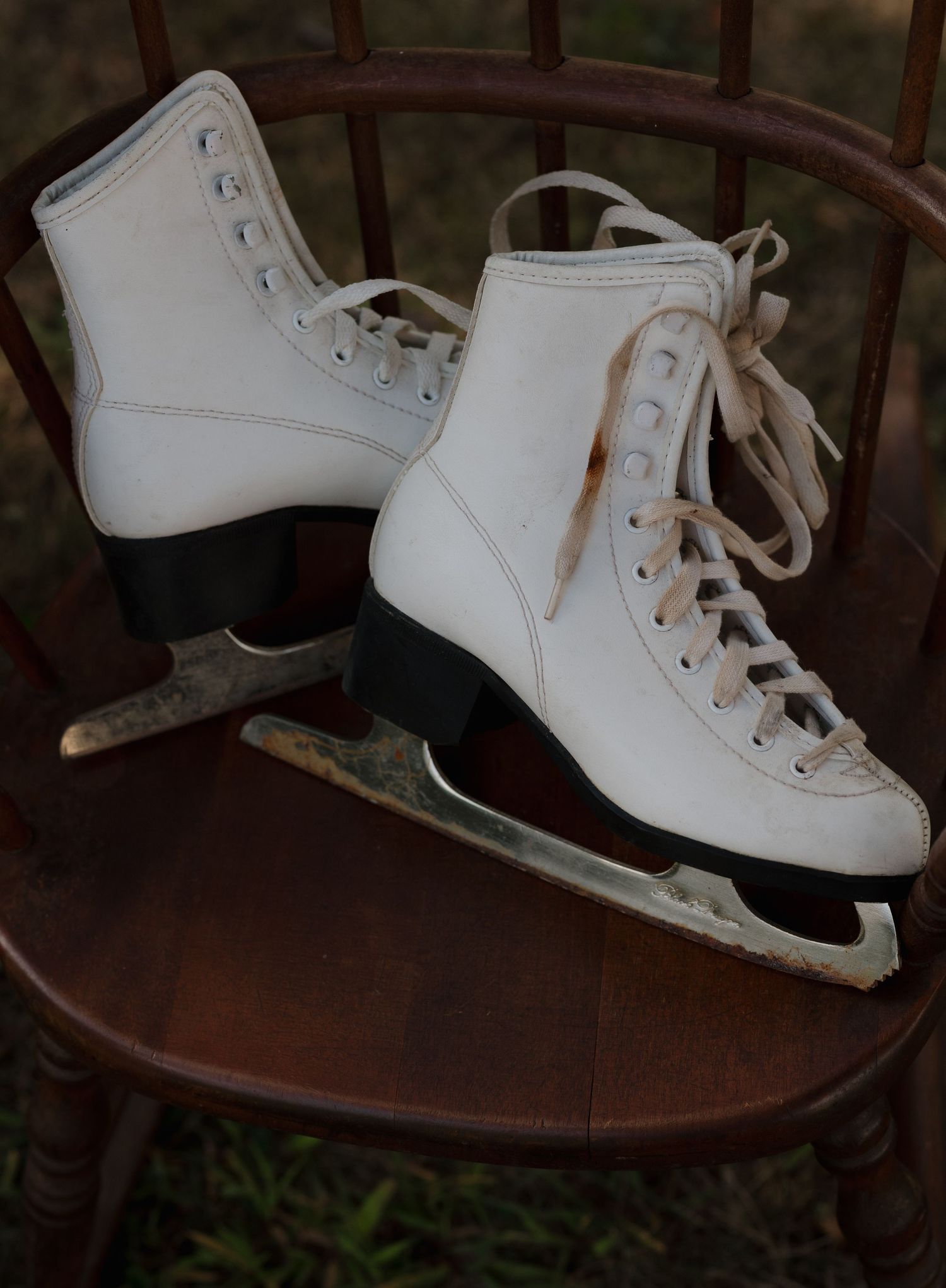 White vintage ice skates displayed on dark wooden furniture.