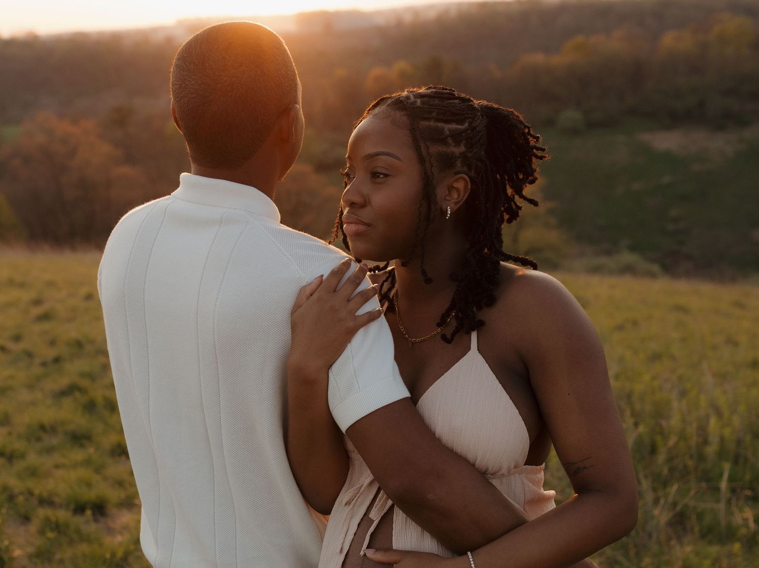 A couple shares a romantic moment at golden hour in a lush green field, the woman gazing up tenderly.