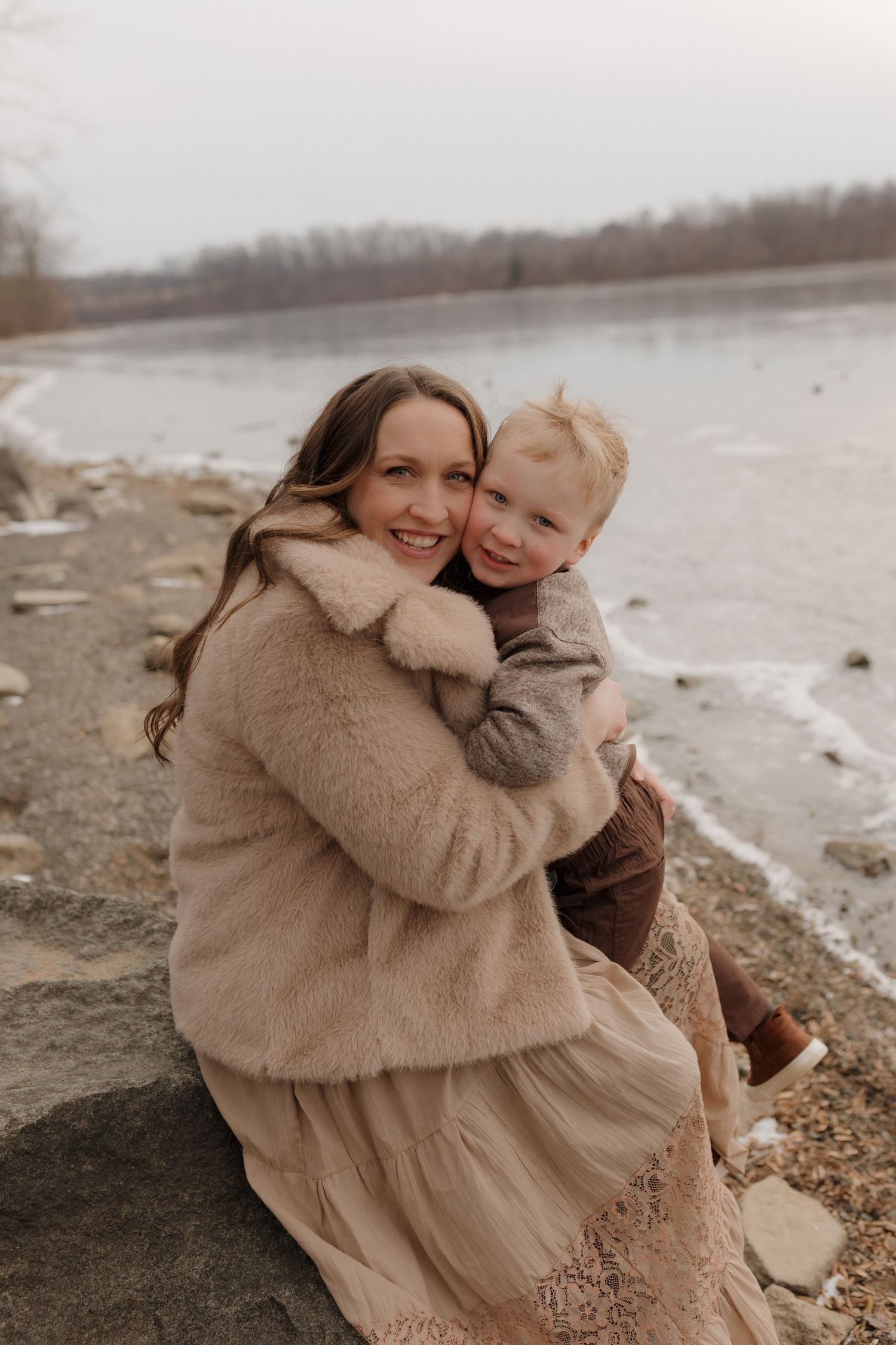 Joyful embraces shared on a winter beach with cloudy skies and water in the background.
