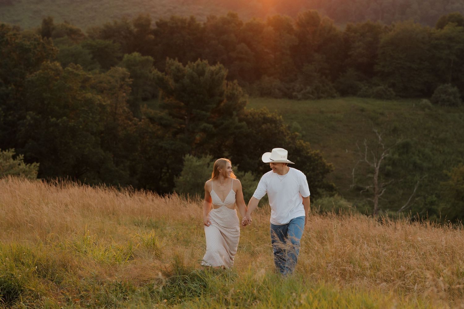 A couple walking hand in hand through a golden field at sunset.
