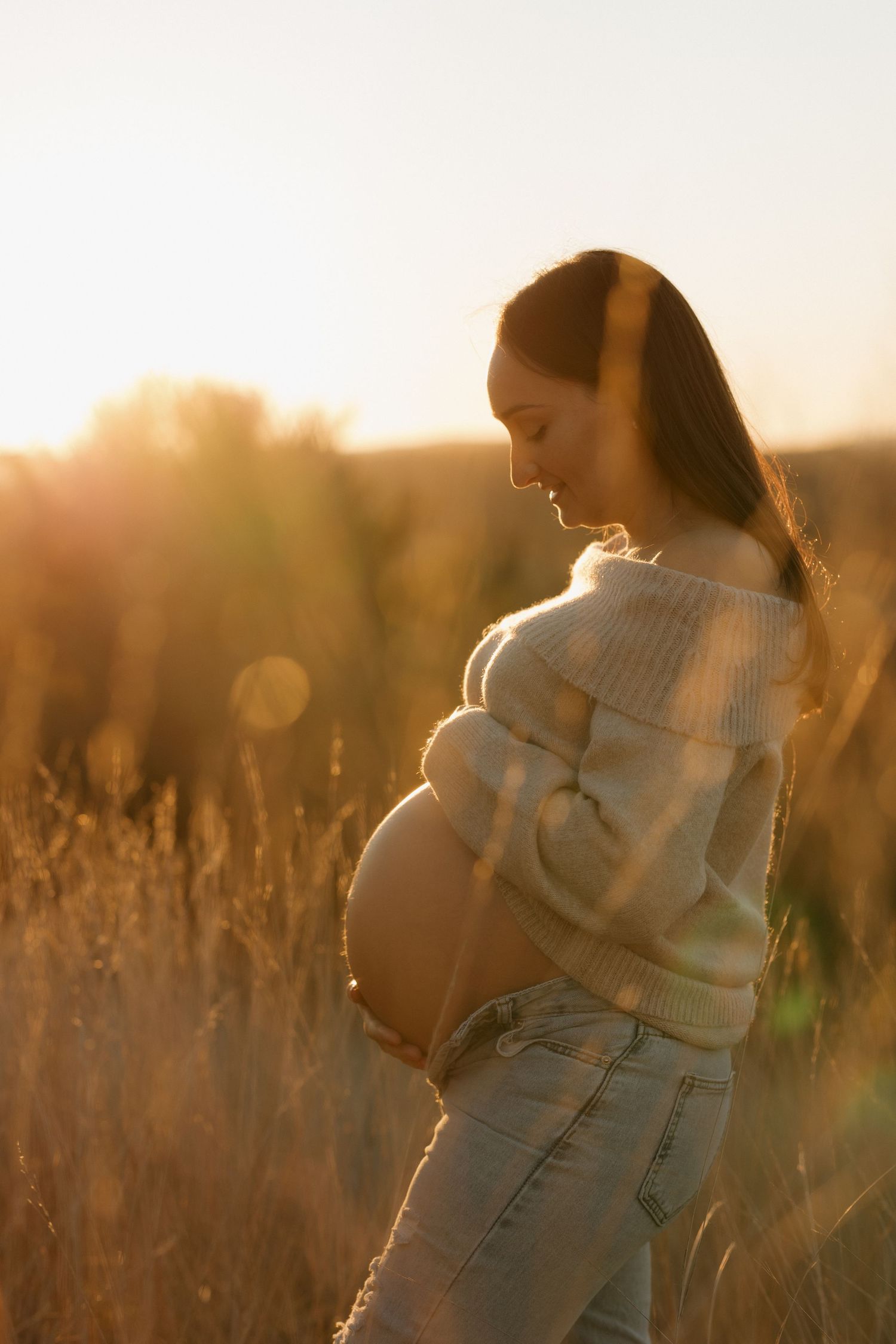 A person in a white sweater cradling their belly in golden sunlit field.