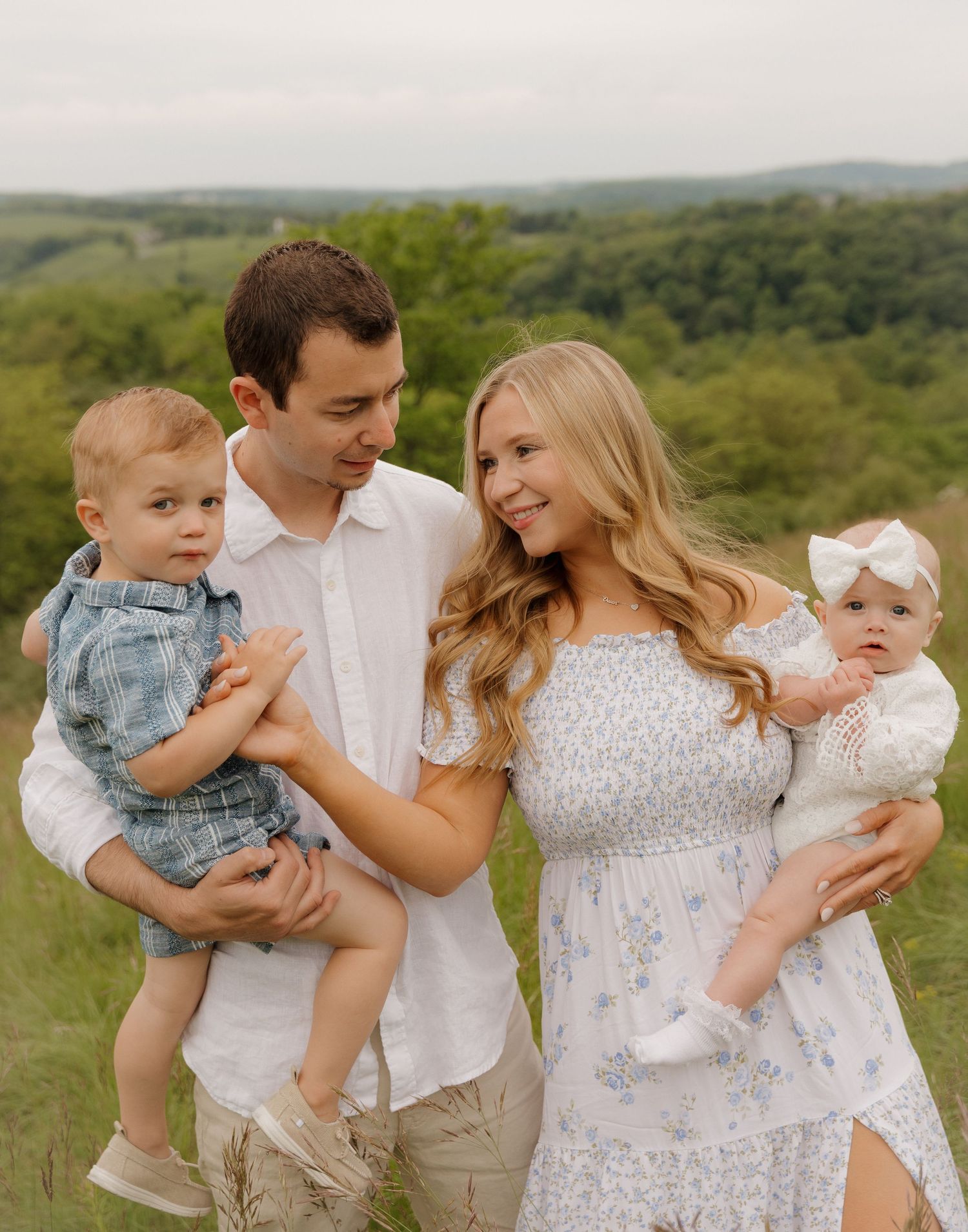 Family shares tender moments together in a series of candid outdoor portraits against a lush green countryside backdrop.
