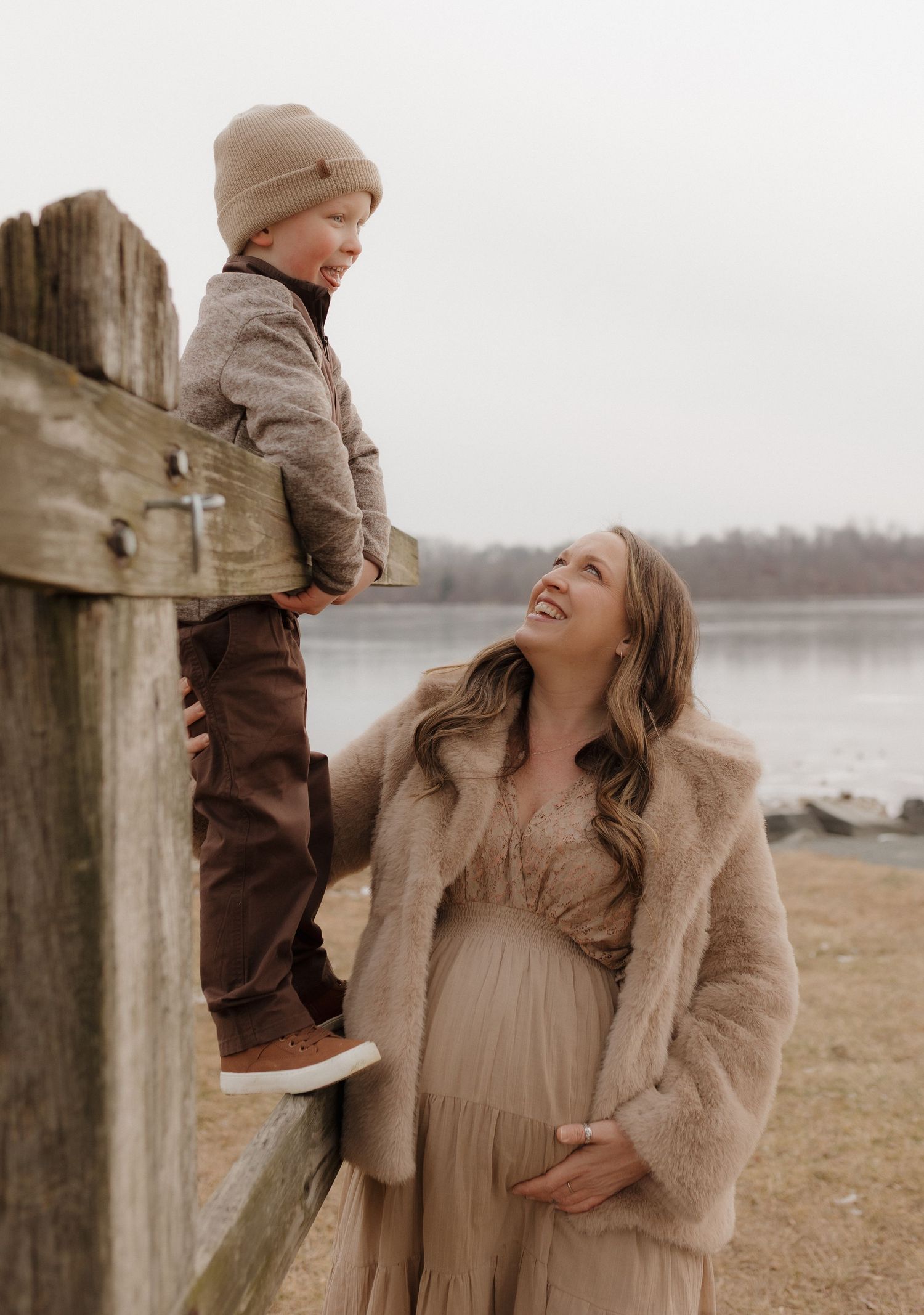 A heartwarming interaction between two people by a wooden fence near a winter lake.