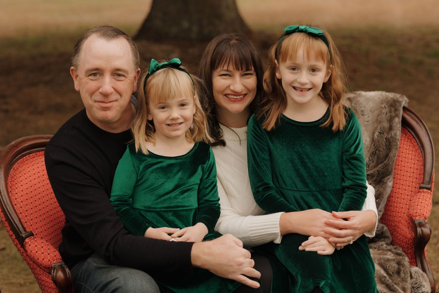 Family sits together on red vintage furniture during outdoor holiday photo session.