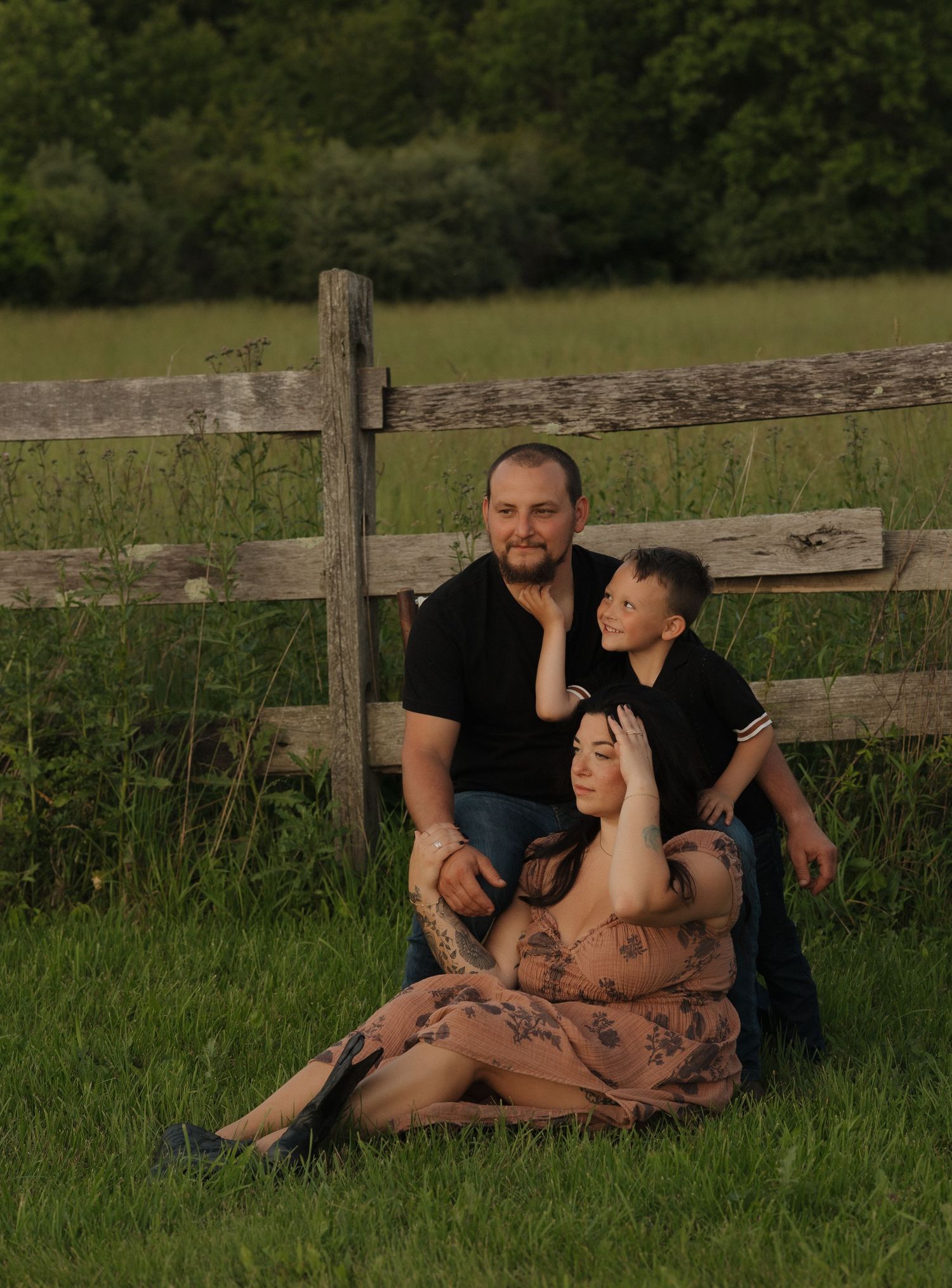 A family sits together by a rustic wooden fence in a green meadow.