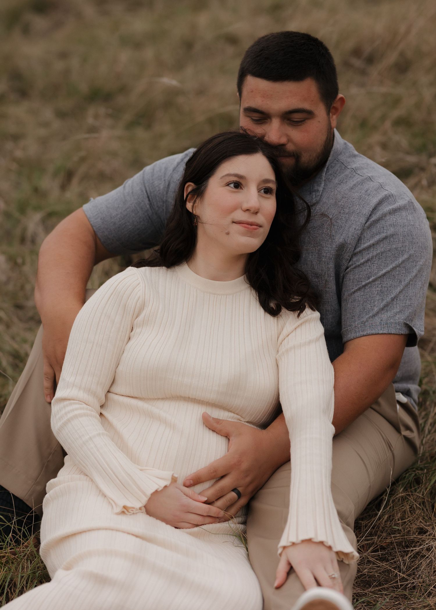 Couple relaxing together on grassy hillside during outdoor photoshoot.