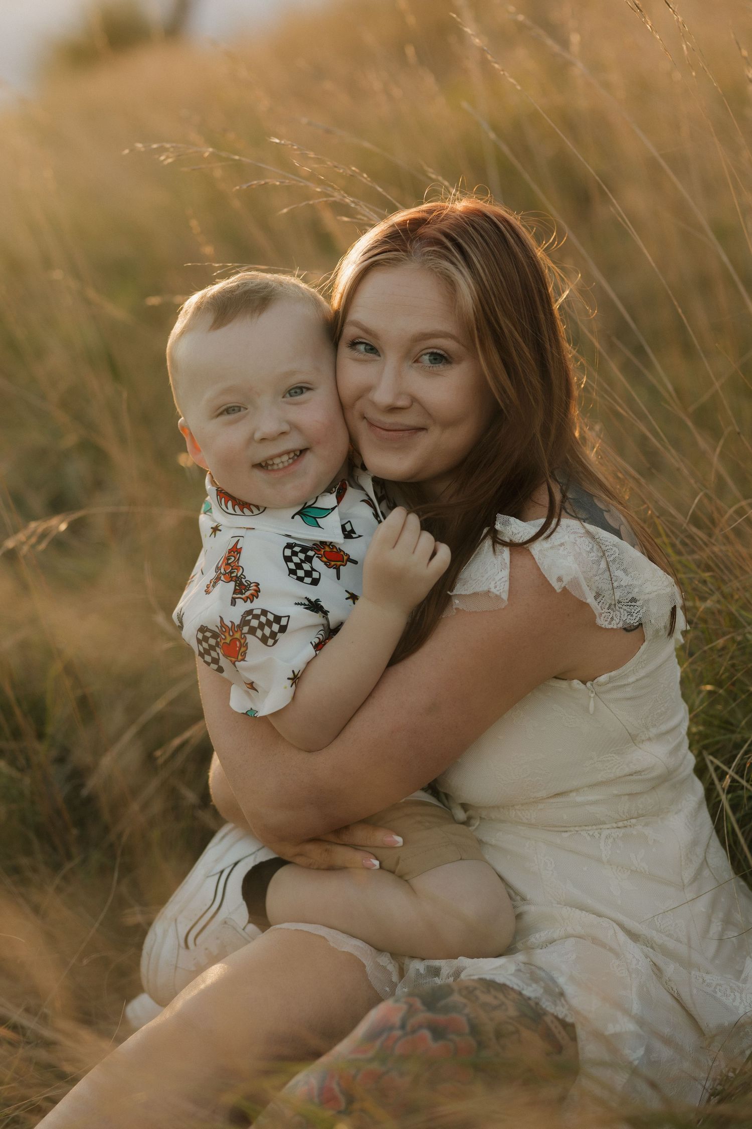Mother and baby share tender moment in golden sunlit field during sunset photoshoot.