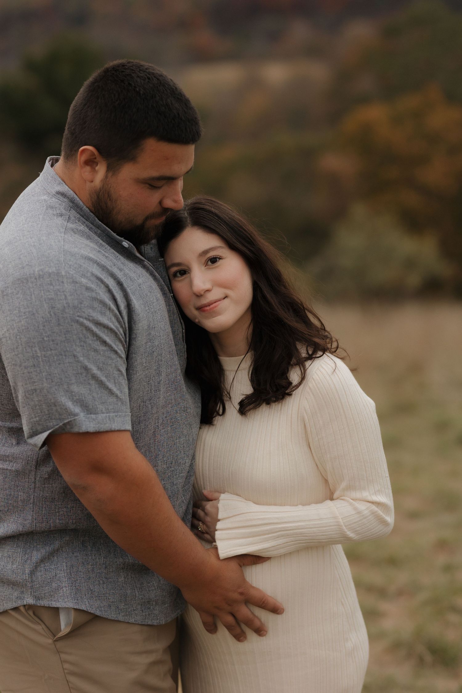 Couple embraces in a natural outdoor setting during maternity photoshoot.