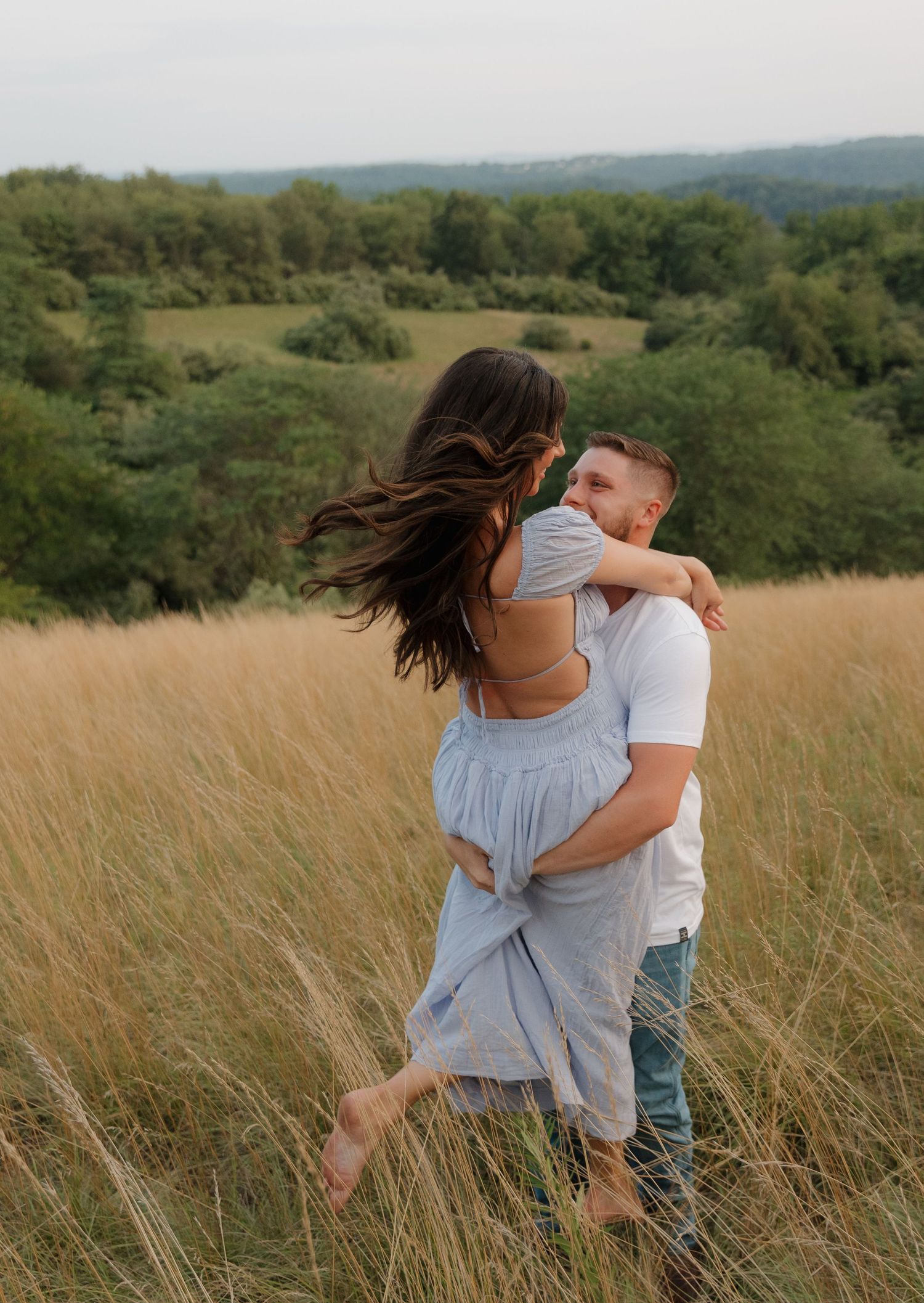 Couple playing and spinning in a field of tall grass during golden hour.
