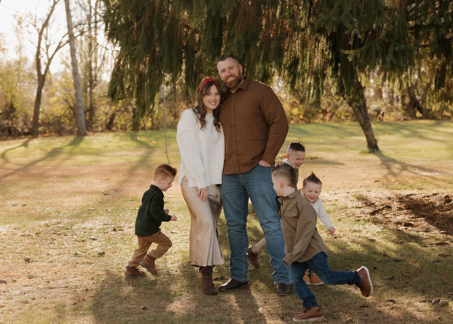 Family playfully interacts under trees in a natural outdoor setting.